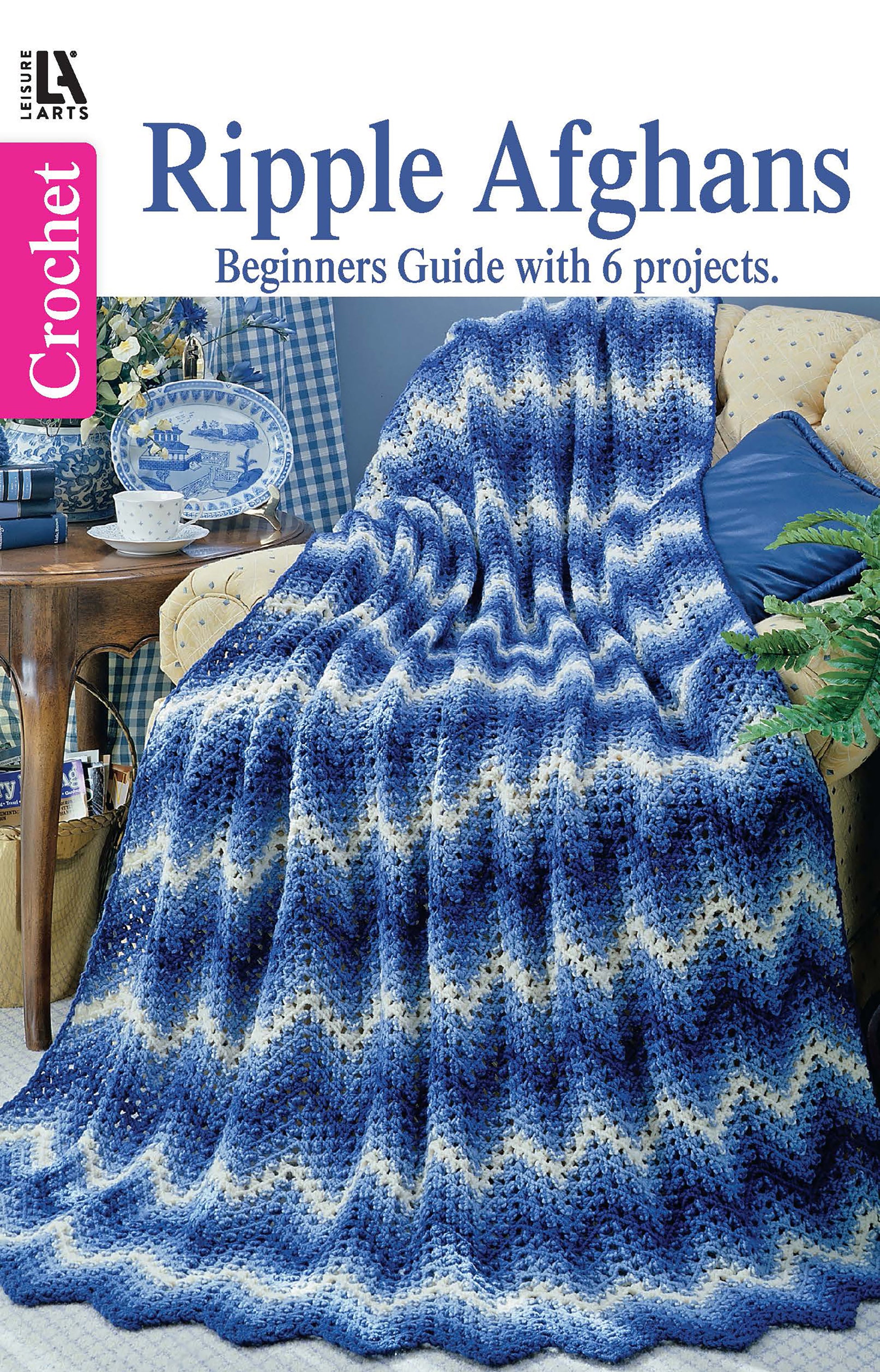 A blue and white crocheted ripple afghan drapes over a beige armchair in a cozy living room. Text: Leisure Arts Beginner's Guide Ripple Afghans Digital Download offers 6 beginner crochet projects and easy patterns.
