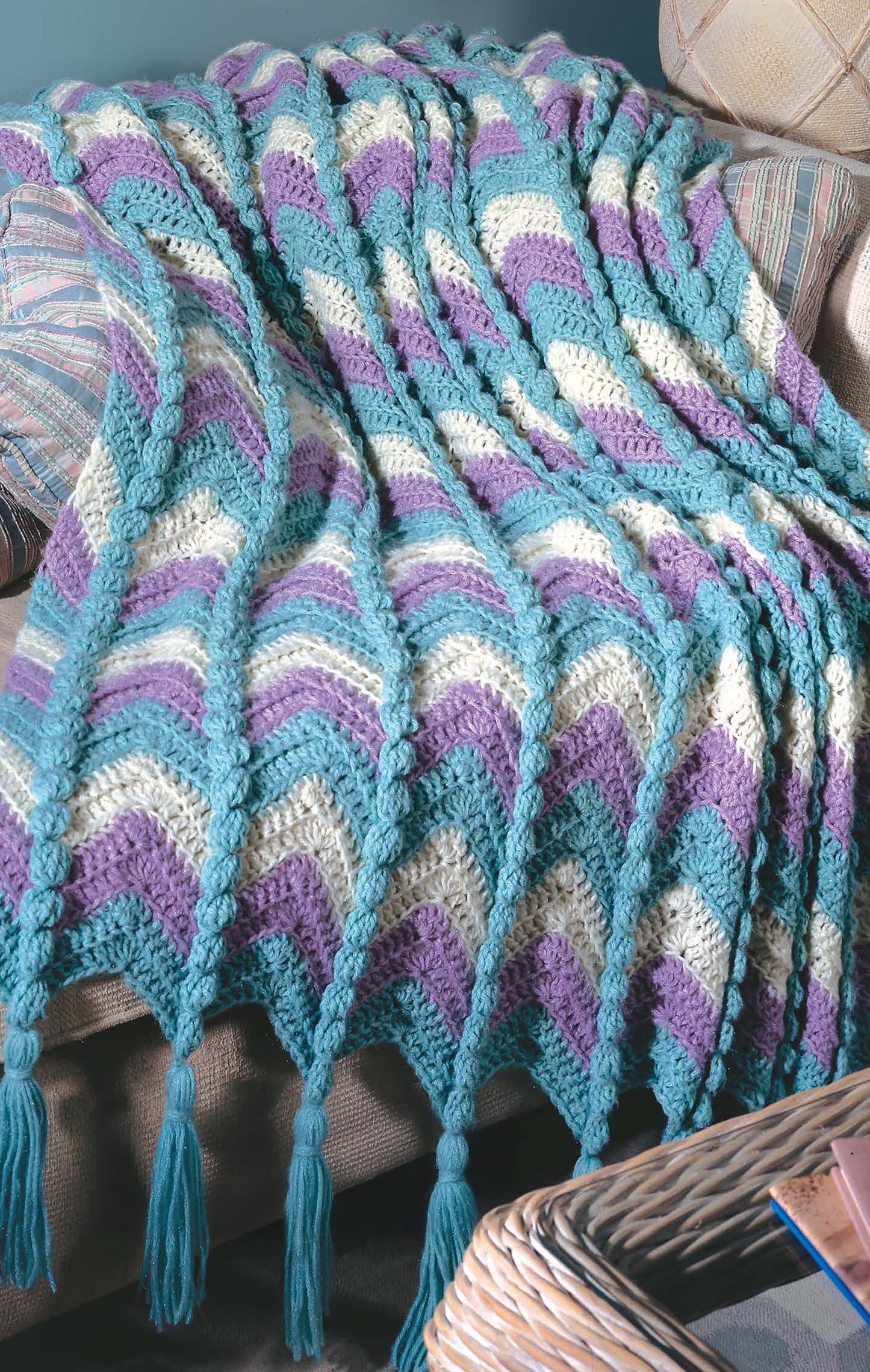 The Leisure Arts Beginner's Guide Ripple Afghans Digital Download features crochet patterns for wavy chevron blankets in teal, cream, and lavender with braided textures and tassel edges—perfect to drape over your sofa.