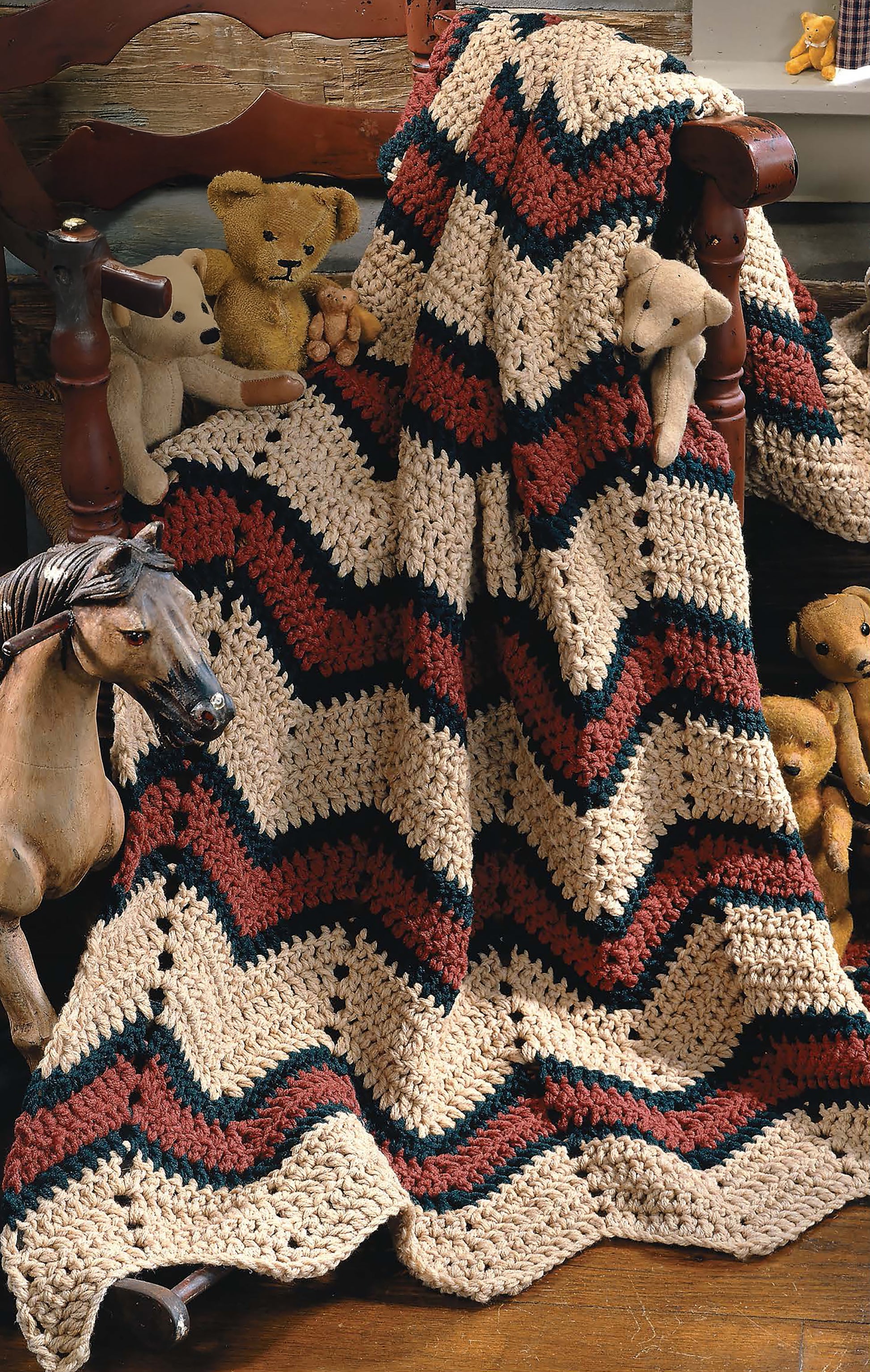 The Beginner's Guide Ripple Afghans Digital Download by Leisure Arts features crochet patterns for a zigzag blanket in cream, brown, and black, perfect for beginners—display it draped on a chair with toys on a wooden floor.
