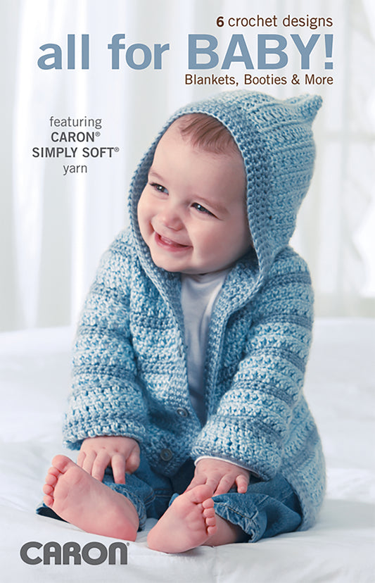 A smiling baby in a blue crocheted hoodie and booties, made with Caron Simply Soft yarn, sits on a white surface. The image promotes All For Baby!—6 Designs by Lori Markovic Digital Download from Leisure Arts.