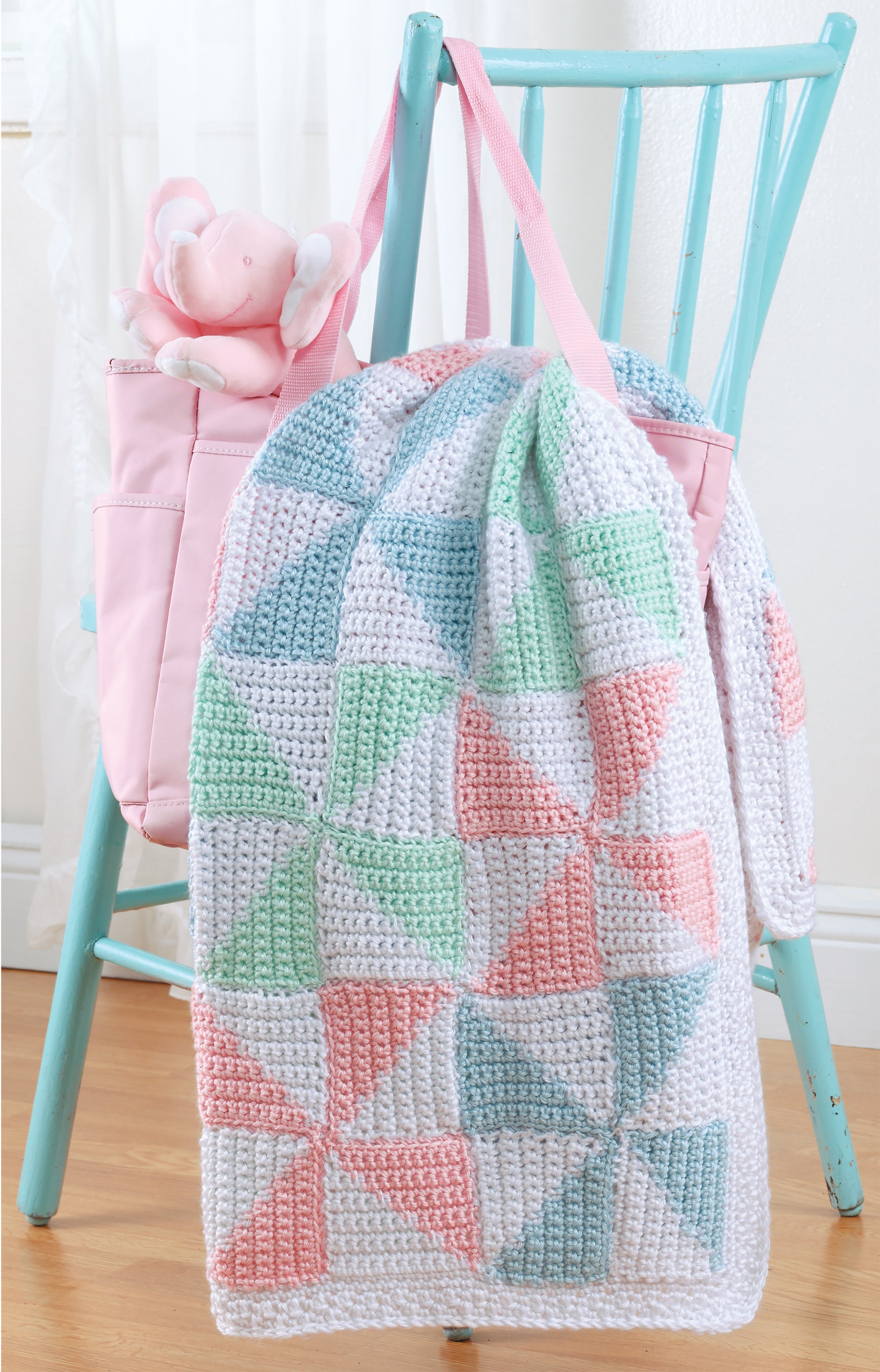 A turquoise chair is draped with a pastel crochet blanket and a pink bag holding a plush bunny, all made using "All For Baby!—6 Designs by Lori Markovic" by Leisure Arts (digital download).