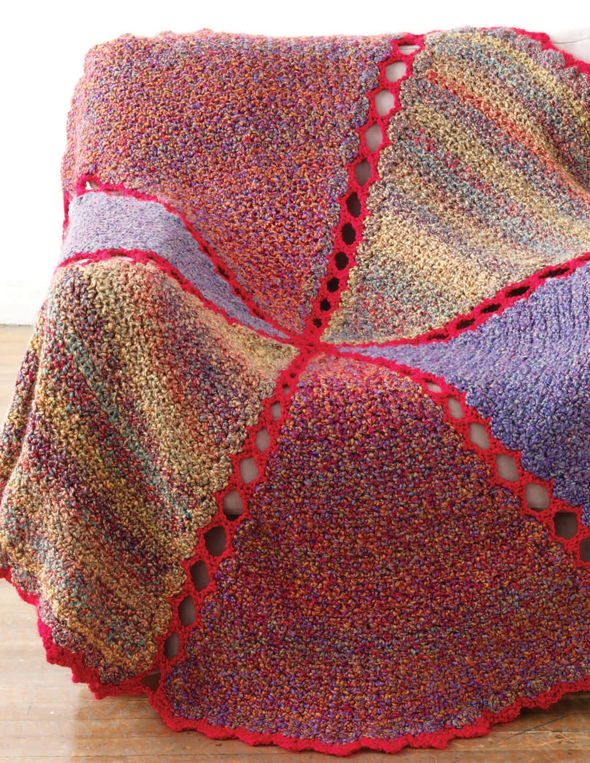 The Great Warm-Ups crochet throw by Leisure Arts features textured, multicolored triangular panels with bright red borders, crafted with afghan patterns and displayed over a surface above a wooden floor.