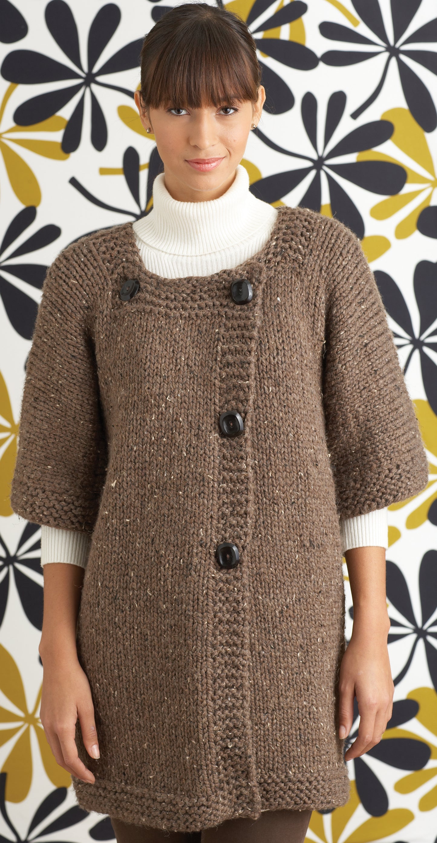 A woman in a chunky brown knit cardigan stands before retro floral wallpaper, highlighting Leisure Arts' "Easy & Quick—4 Knit & 2 Crochet Designs" made with Lion Brand Wool-Ease Thick & Quick (digital download).