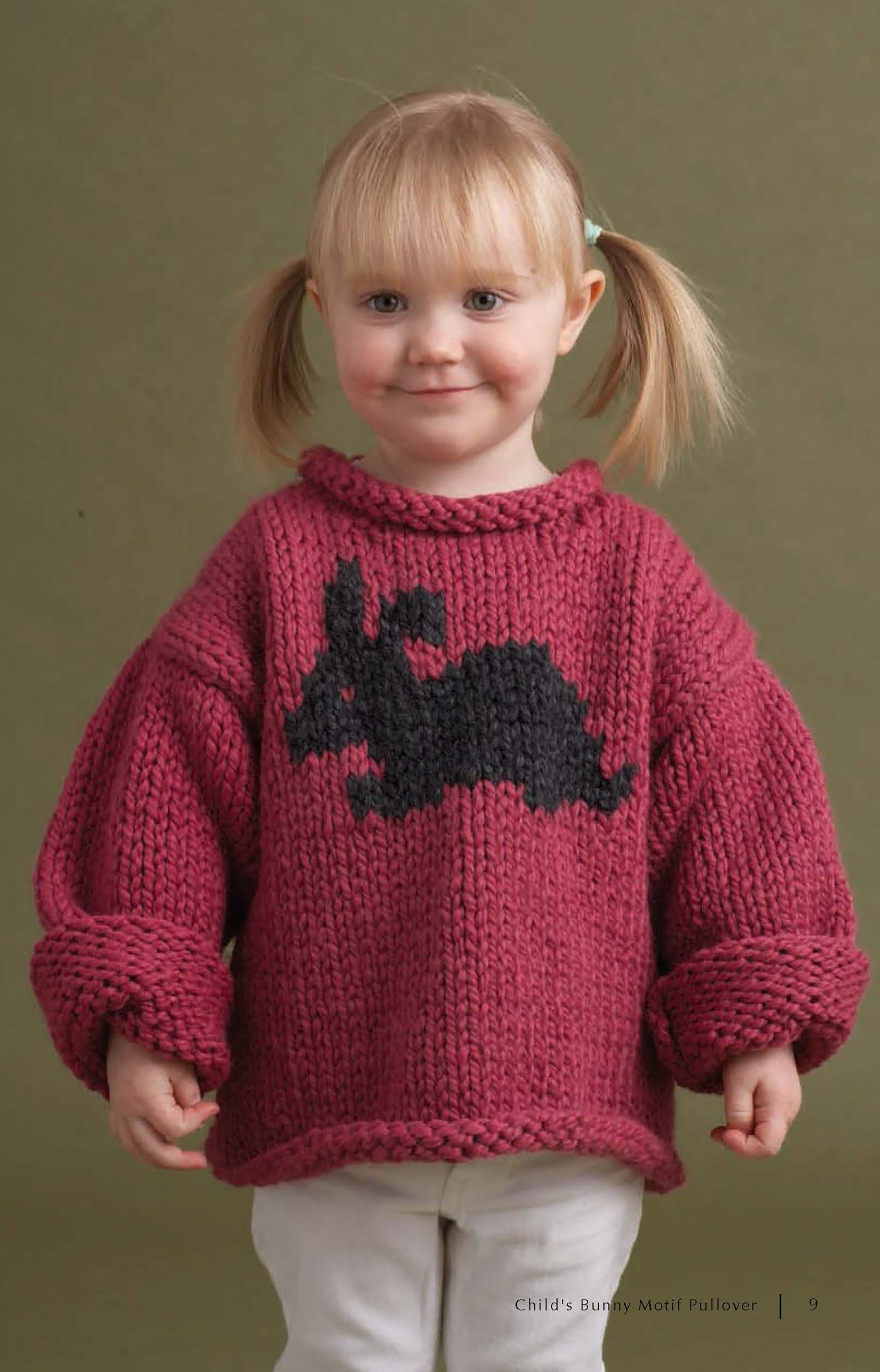 A young child with blonde pigtails wears a chunky maroon sweater featuring a black bunny, made using patterns from Super Cute Super Quick Crochet by Leisure Arts, and smiles against an olive-green background.