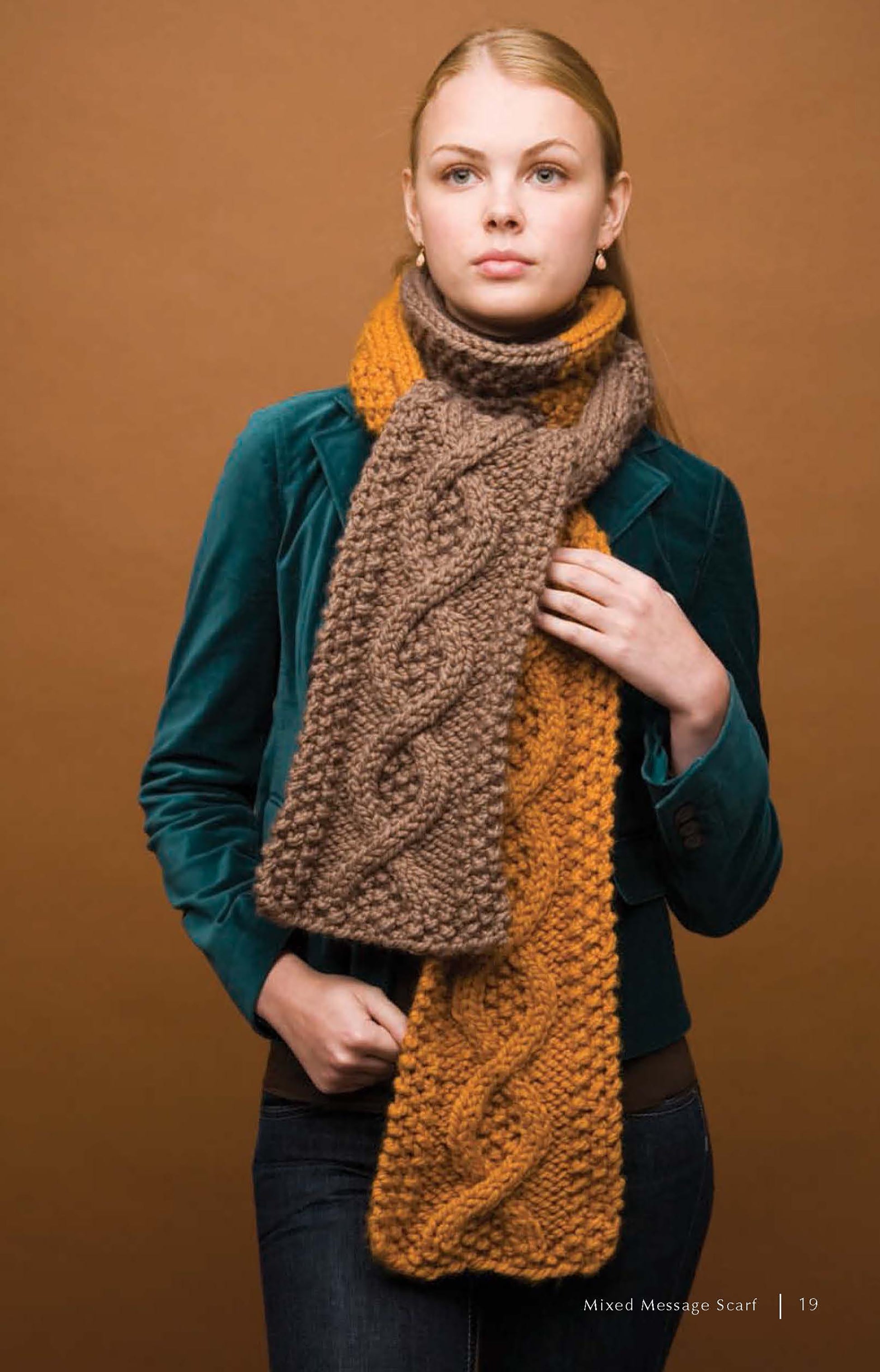 A woman in a teal jacket and jeans models a chunky cable-patterned brown and mustard yellow scarf, made with instructions from “Super Cute Super Quick Crochet” by Leisure Arts—ideal for beginners wanting cozy crochet designs.