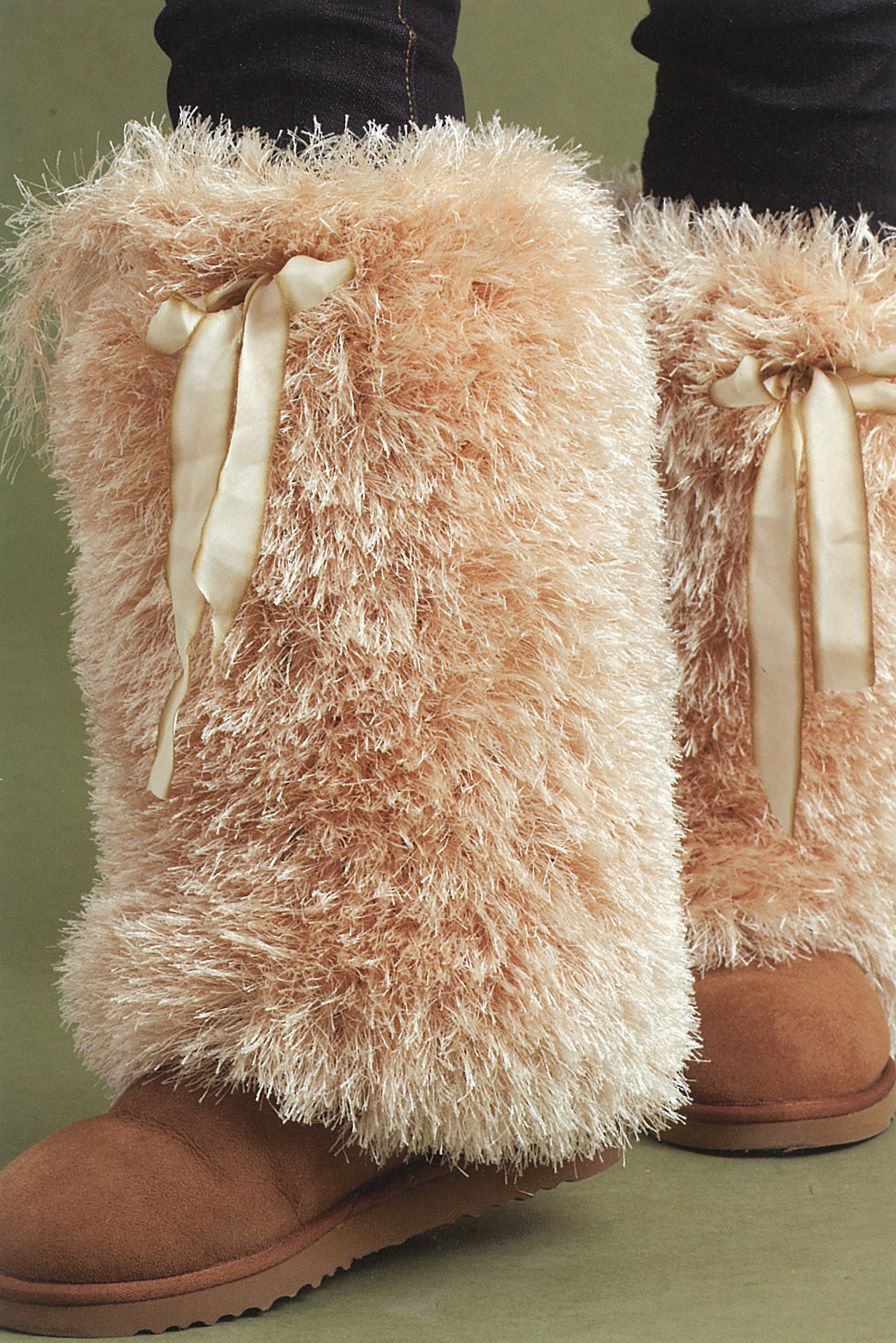 Lion Brand Yarn's Absolutely Fun Fur Digital Download by Leisure Arts is showcased with tan furry boots and shiny cream ribbons over black leggings on a green background—great for pairing with cozy knits or faux fur scarves.