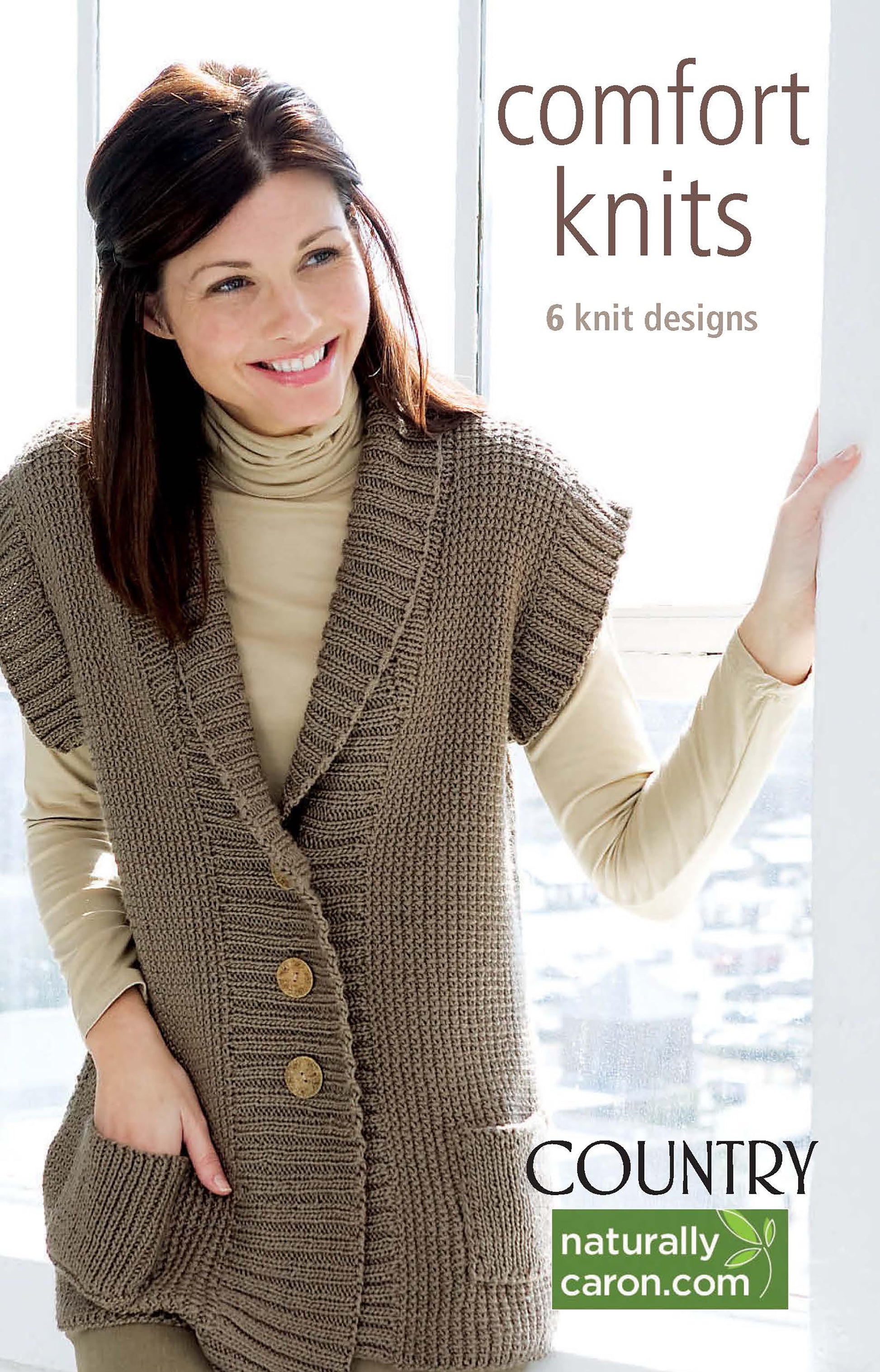 A woman in a tan turtleneck and chunky brown vest stands by a window. Text: Comfort Knits—6 Knit Designs; Caron Country by Leisure Arts. Includes knit sweater patterns using worsted weight yarn. NaturallyCaron.com.