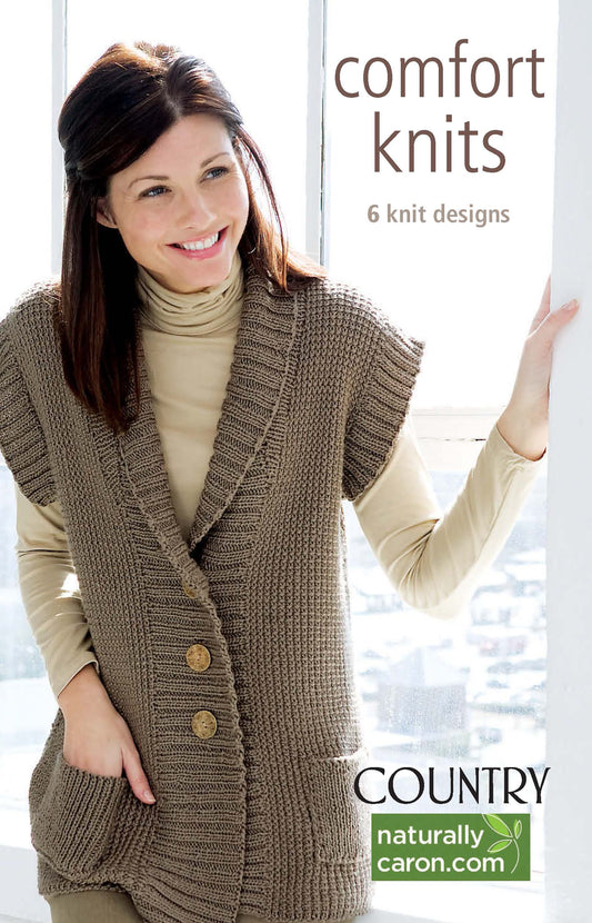 A woman in a tan turtleneck and chunky brown vest stands by a window. Text: Comfort Knits—6 Knit Designs; Caron Country by Leisure Arts. Includes knit sweater patterns using worsted weight yarn. NaturallyCaron.com.