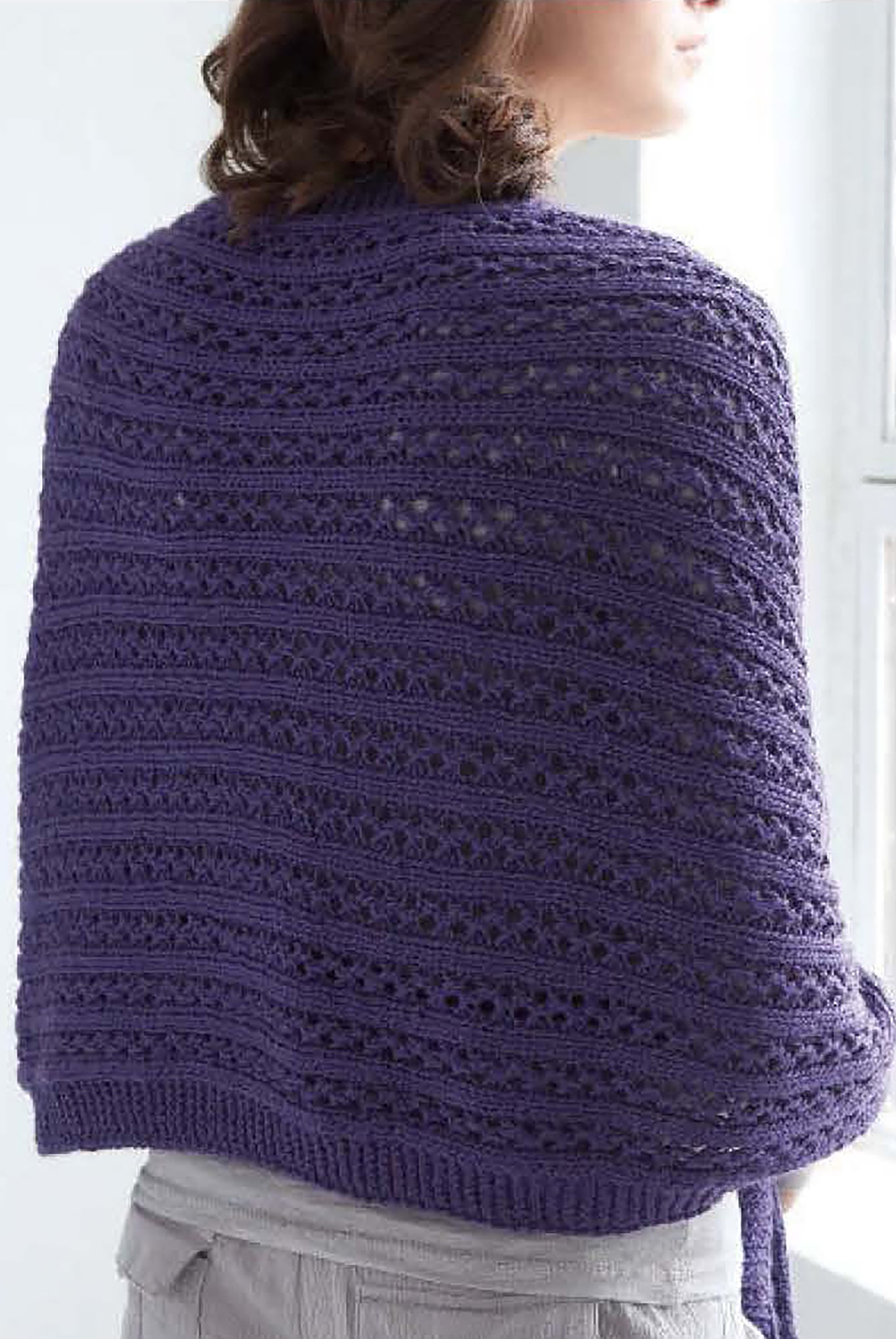 A person wears a textured, lacy purple shawl from Comfort Knits—6 Knit Designs by Caron Country, Leisure Arts. Crafted with worsted yarn, it's ideal for those who love unique shawl knitting patterns and handmade style.