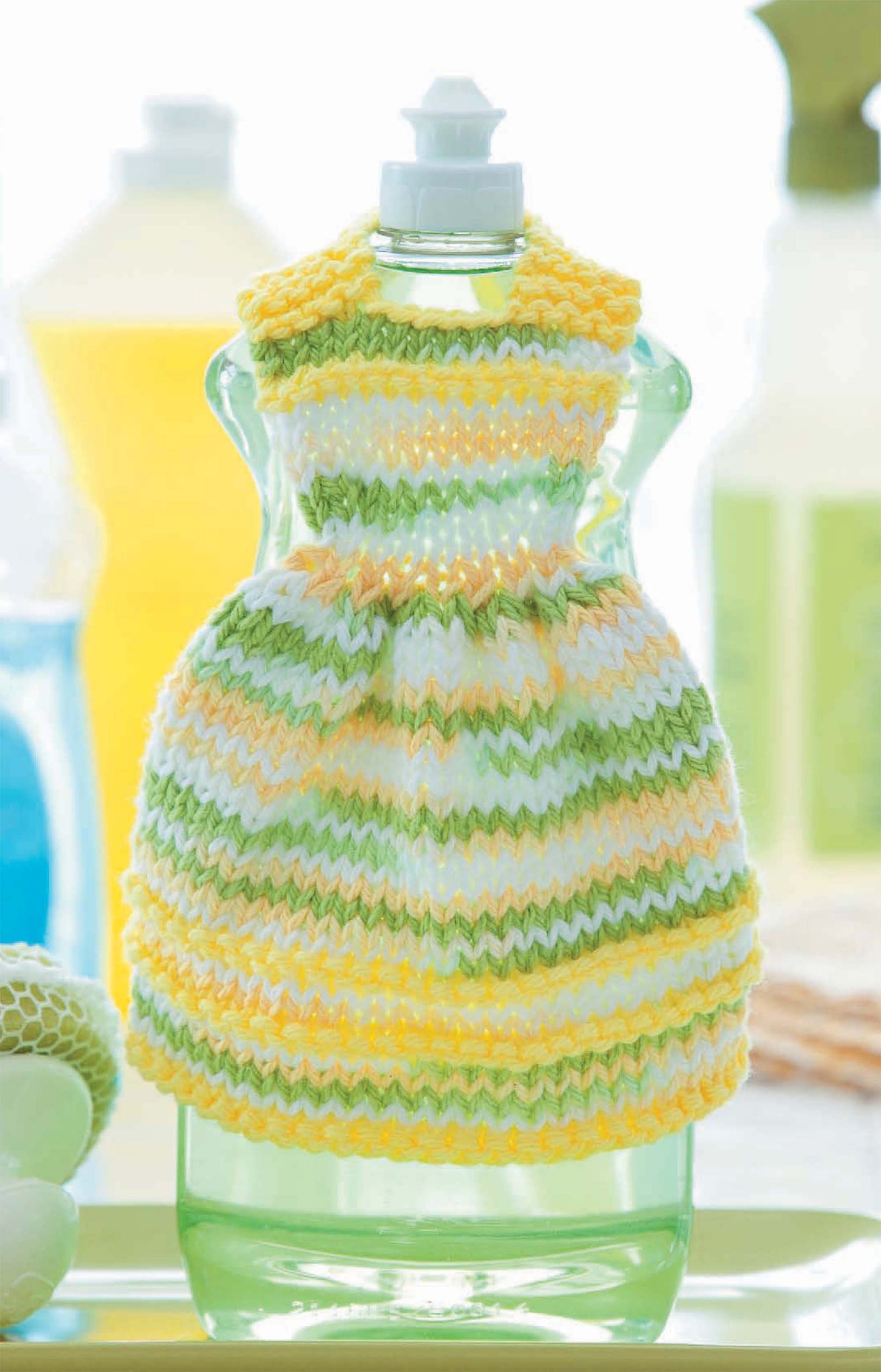 The Leisure Arts "Dishcloth Dresses—The Cutest Quick & Easy Gifts, Ever!" digital download features a dish detergent bottle cover styled like a doll’s outfit in a knitted yellow, green, and white cotton-striped dress.