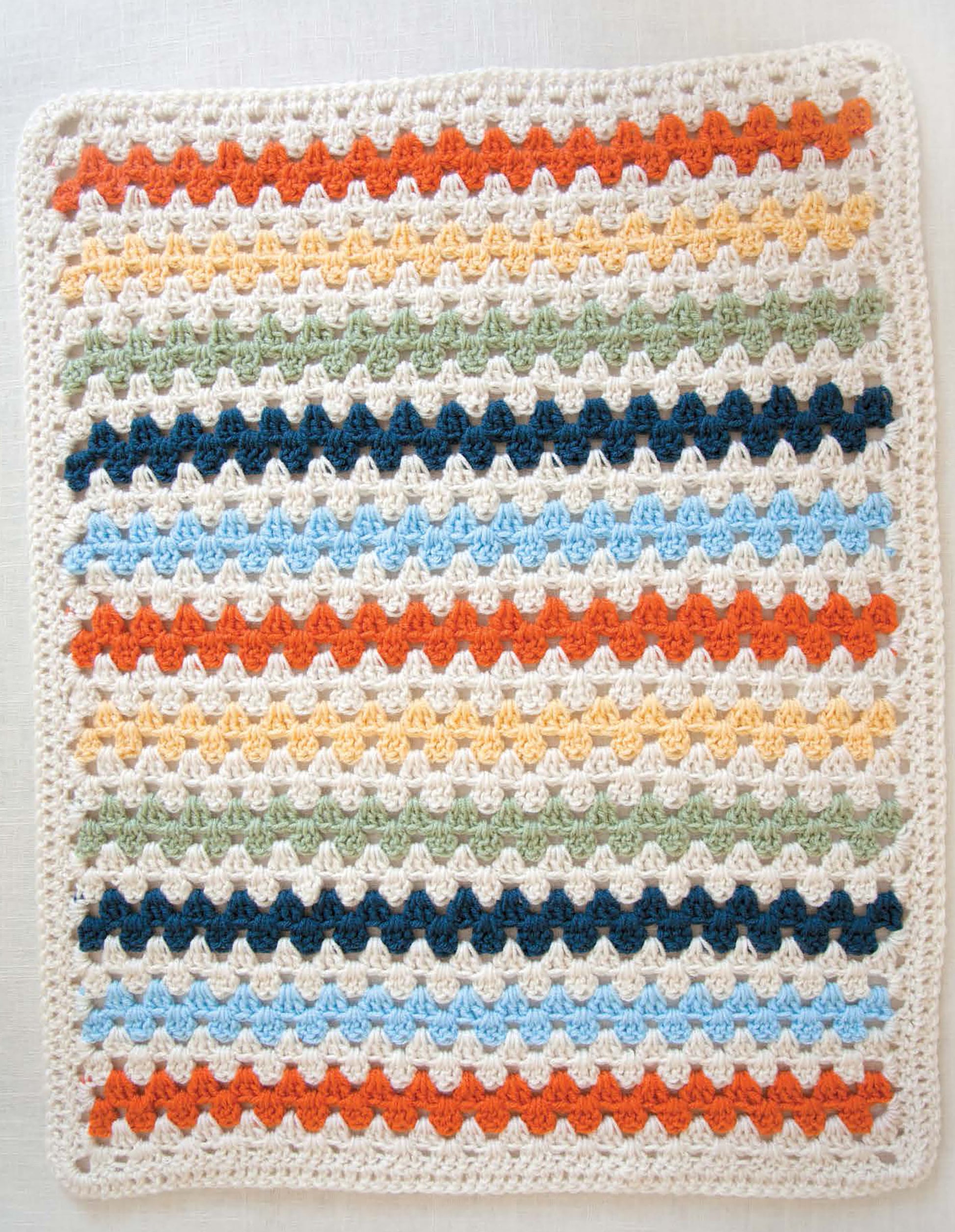 The Leisure Arts Baby Afghans—Cuddly Wraps for Babies & Toddlers! features a cozy crocheted blanket with wavy scalloped stripes in cream, orange, light blue, green, and navy, bordered in cream—perfect for beginners seeking easy crochet patterns.