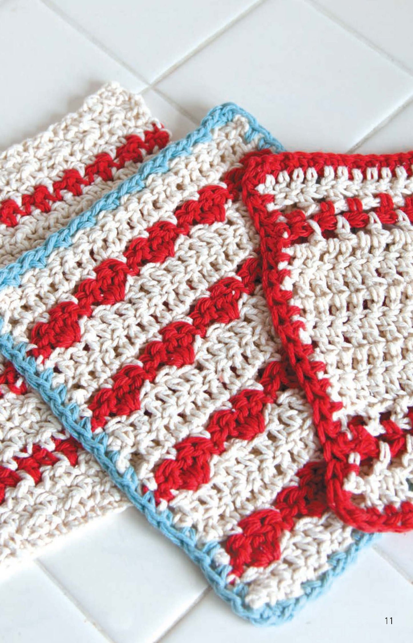 Leisure Arts Dishcloths—two crocheted cotton pieces in cream and red diagonal stripes with a light blue border—rest on white tile. Ideal for beginners seeking new crochet patterns or easy projects.