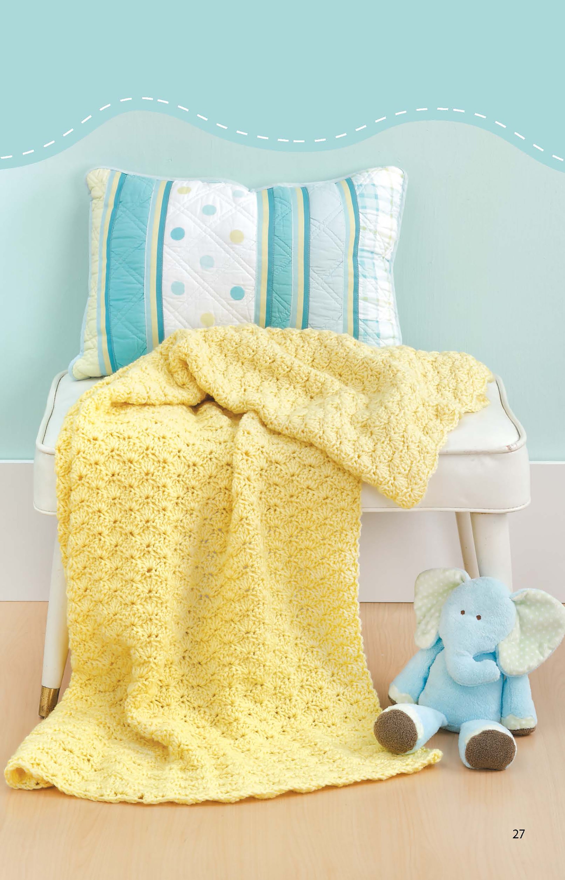 The Leisure Arts Crochet Blankets for Toddlers, in soft yellow medium-weight yarn, is draped over a white chair with a striped pillow, beside a blue stuffed elephant on a light wood floor and mint green wall.