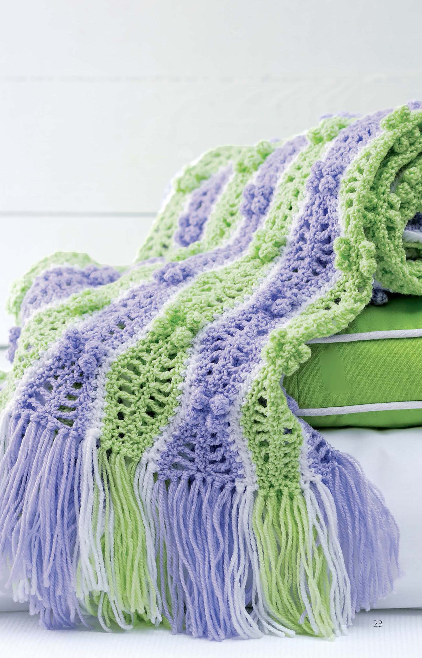 The Learn to Make Mile-a-Minute Baby Afghans by Leisure Arts features beginner-friendly crochet patterns with wavy stripes in pastel green, lavender, and white, plus a fringe edge and charming textured details. Digital download. Draped on a green cushion.