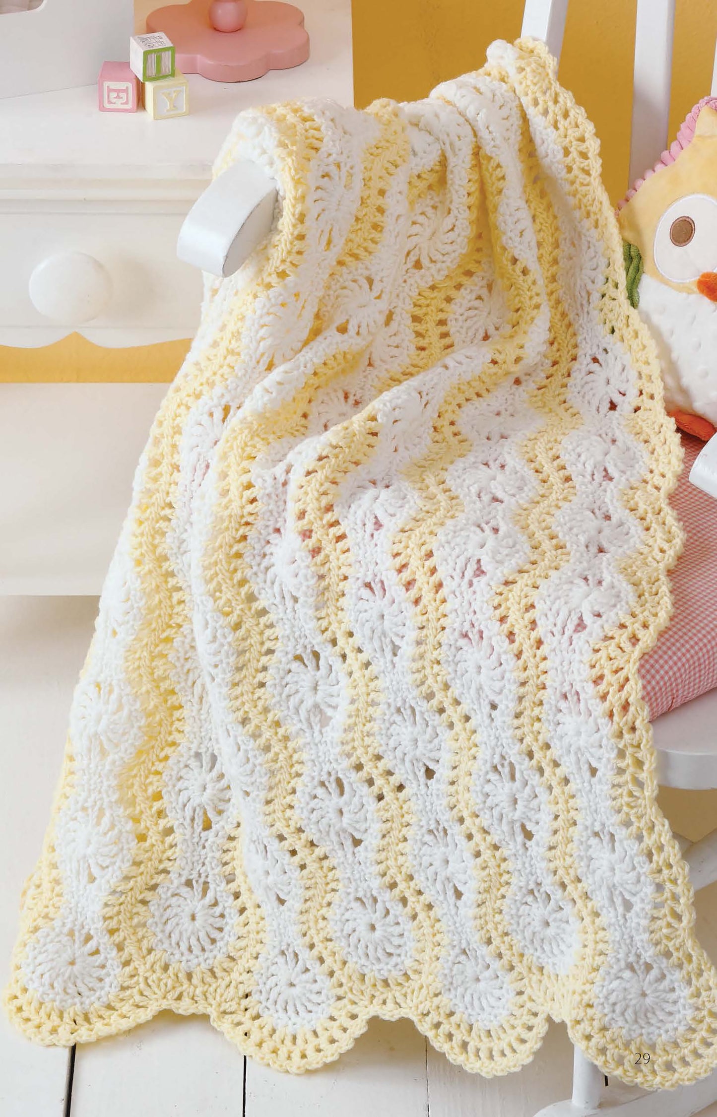 The "Learn to Make Mile-a-Minute Baby Afghans" digital download by Leisure Arts is displayed draped over a white chair in soft yellow and white stripes, next to a stuffed owl—perfect for beginner crochet projects.