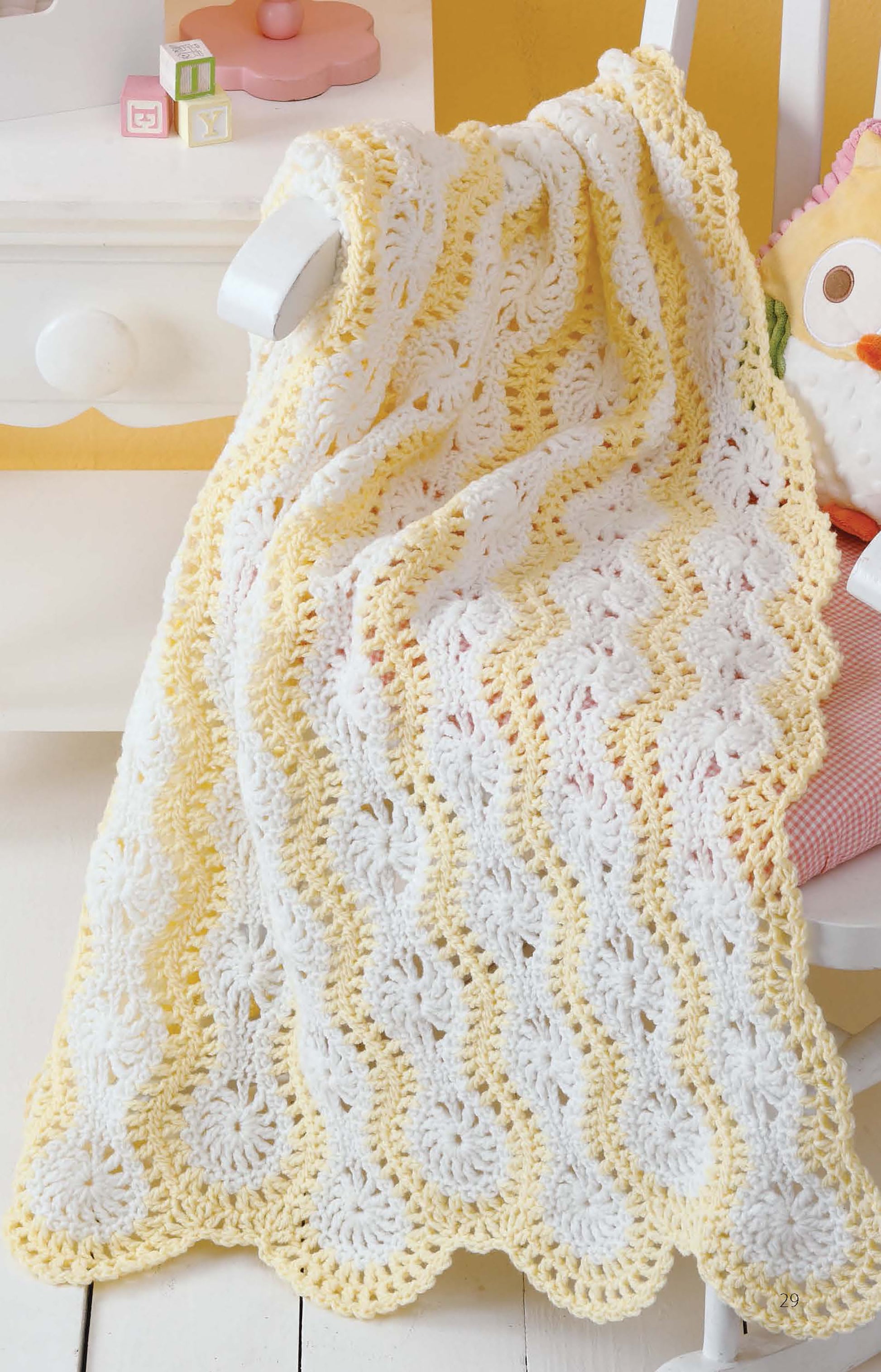 The "Learn to Make Mile-a-Minute Baby Afghans" digital download by Leisure Arts is displayed draped over a white chair in soft yellow and white stripes, next to a stuffed owl—perfect for beginner crochet projects.