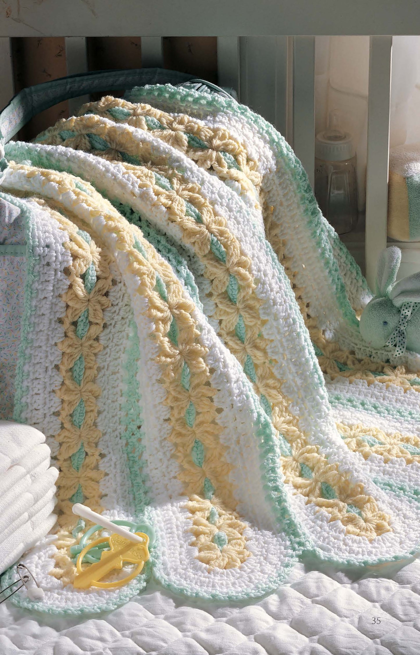 The Leisure Arts "Learn to Make Mile-a-Minute Baby Afghans" digital download shows a crocheted striped baby blanket in white, yellow, and mint green draped over a crib with baby accessories like a green stuffed rabbit and towels.
