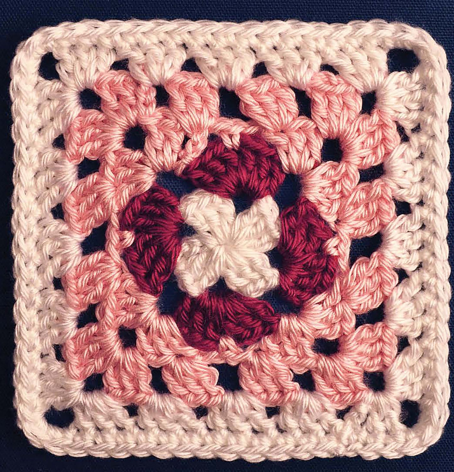 Perfect for beginners, the Leisure Arts Complete Guide to Symbol Crochet features a granny square with a white center, dark pink ring, light pink rounds, and white border—ideal for practicing basic stitches on a dark blue background.