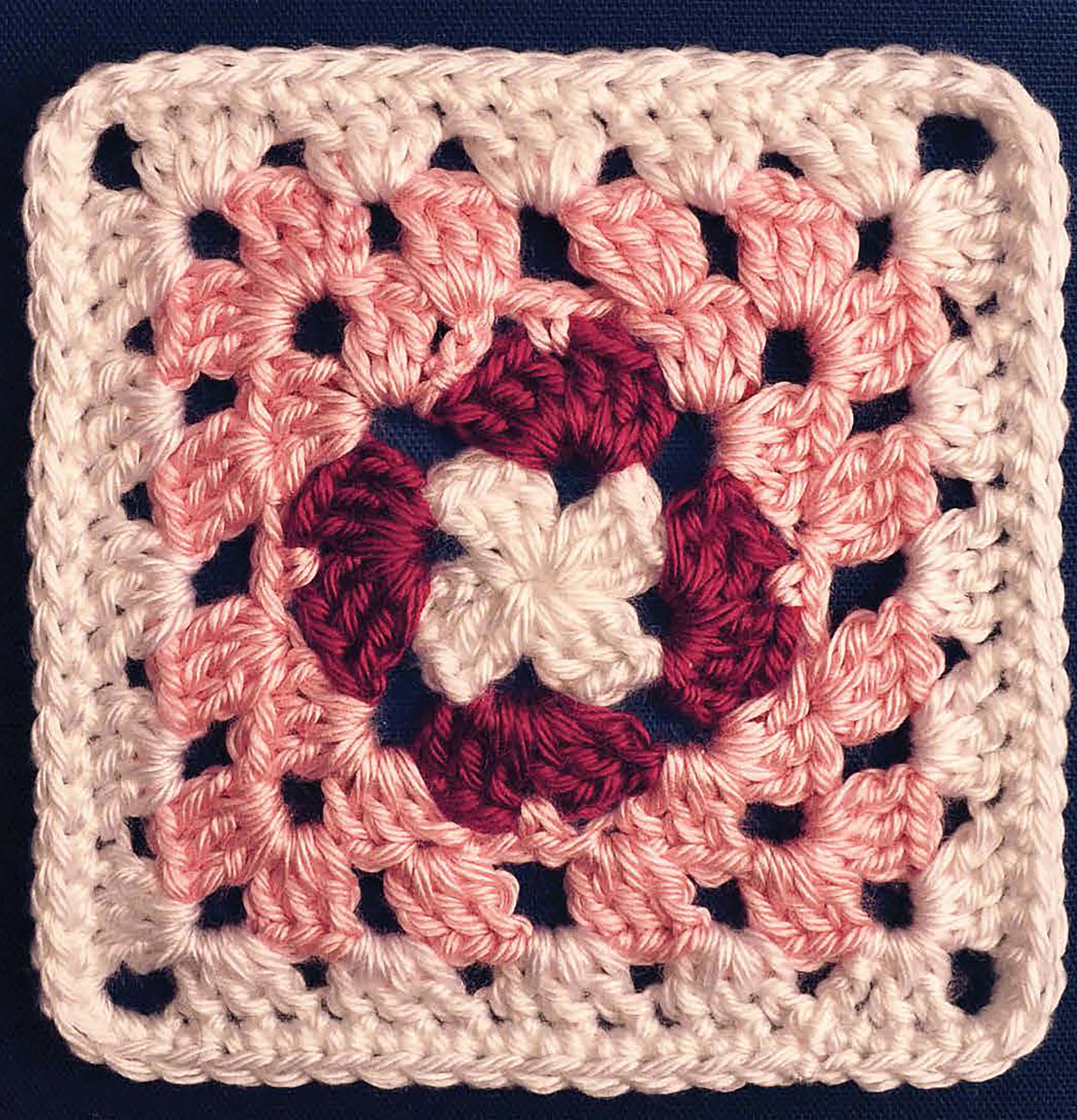 Perfect for beginners, the Leisure Arts Complete Guide to Symbol Crochet features a granny square with a white center, dark pink ring, light pink rounds, and white border—ideal for practicing basic stitches on a dark blue background.
