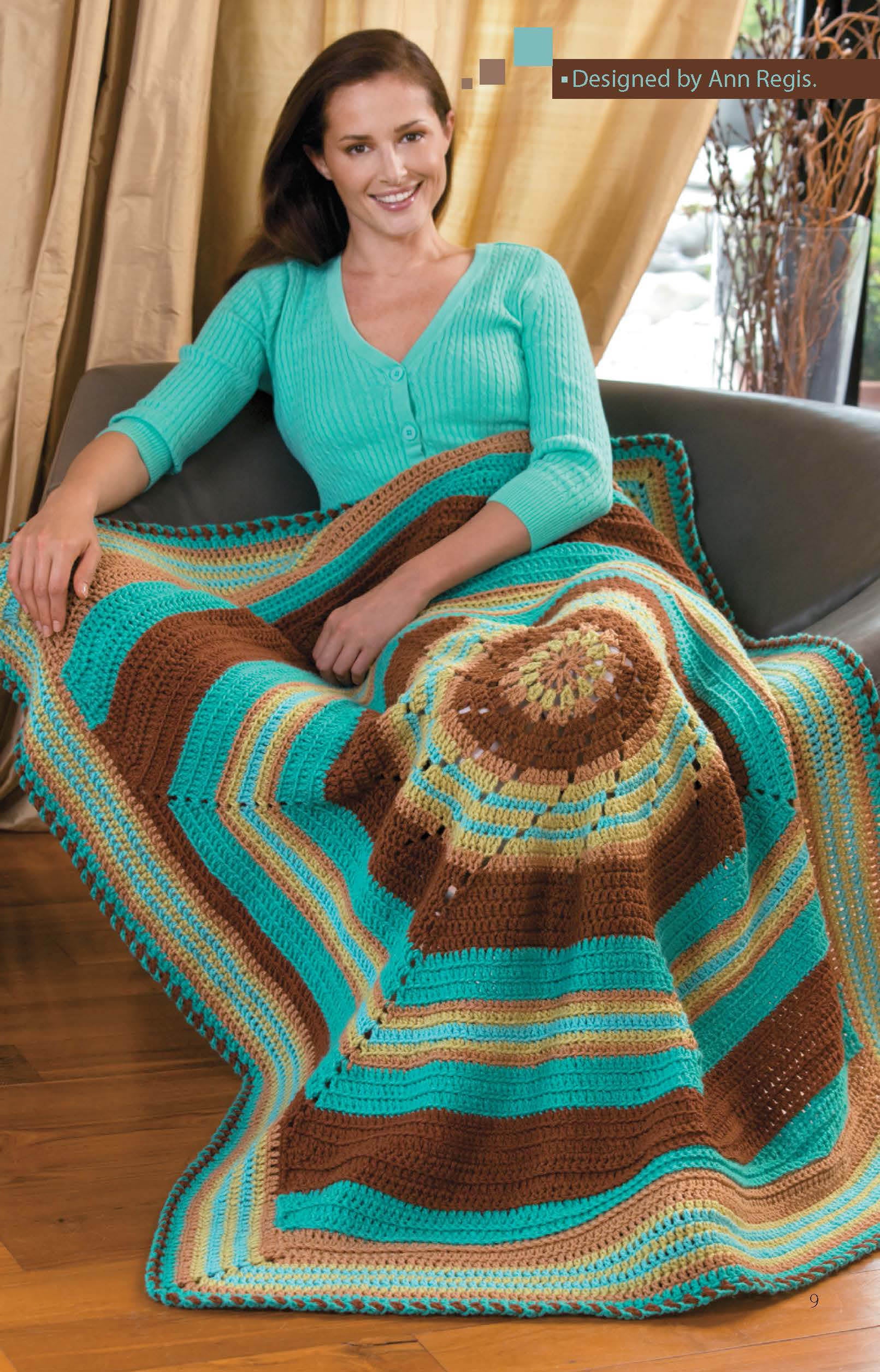 A woman smiles on a gray couch, wrapped in a colorful afghan made with Leisure Arts' "Crochet Throws Worked in the Round" digital pattern—ideal for easy to intermediate crochet enthusiasts.