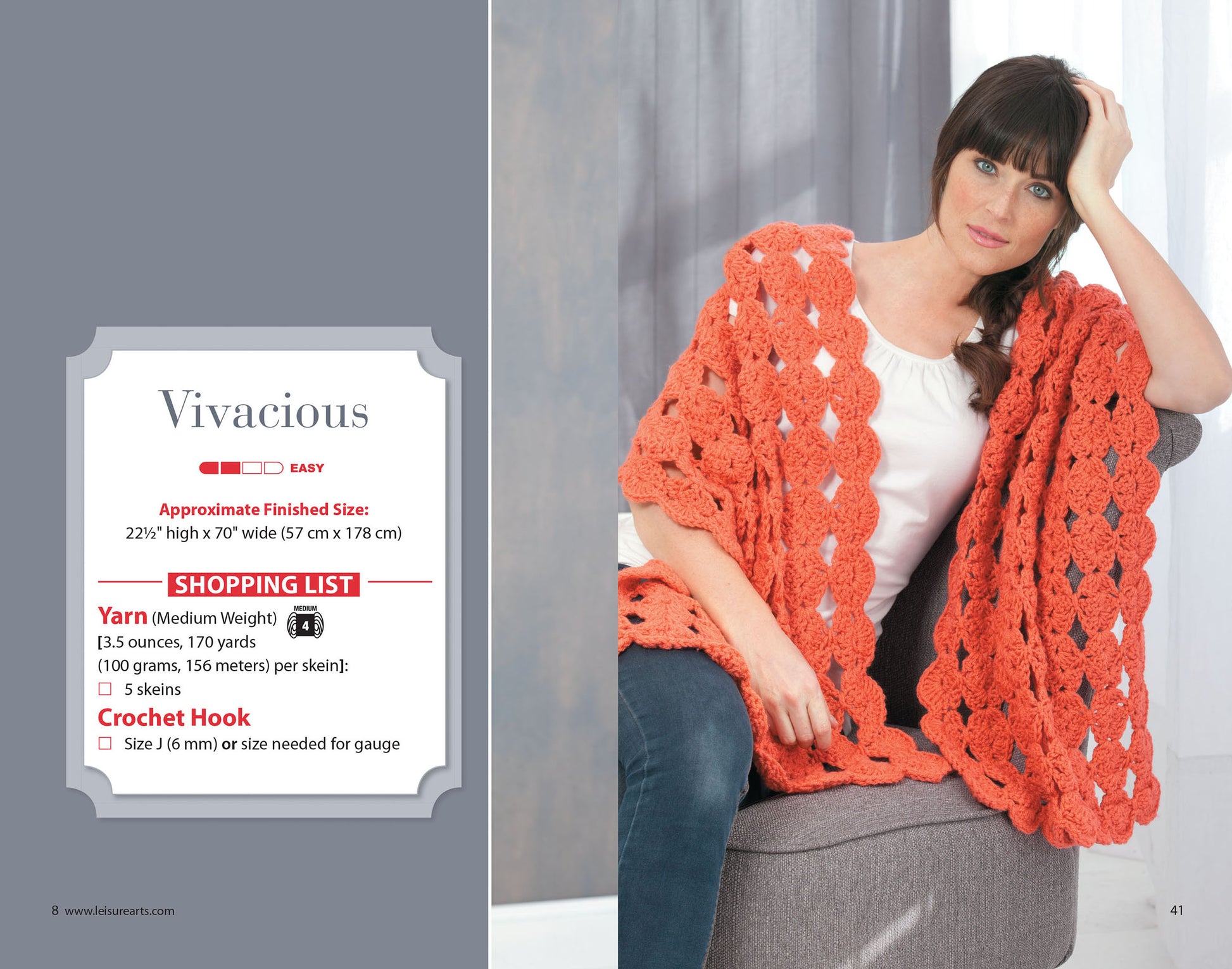A woman with brown hair sits on a gray chair, draped in a chunky coral shawl she crocheted from Everyday Shawls by Leisure Arts, with the pattern book, project notes, and a shopping list for beginner crochet supplies beside her.