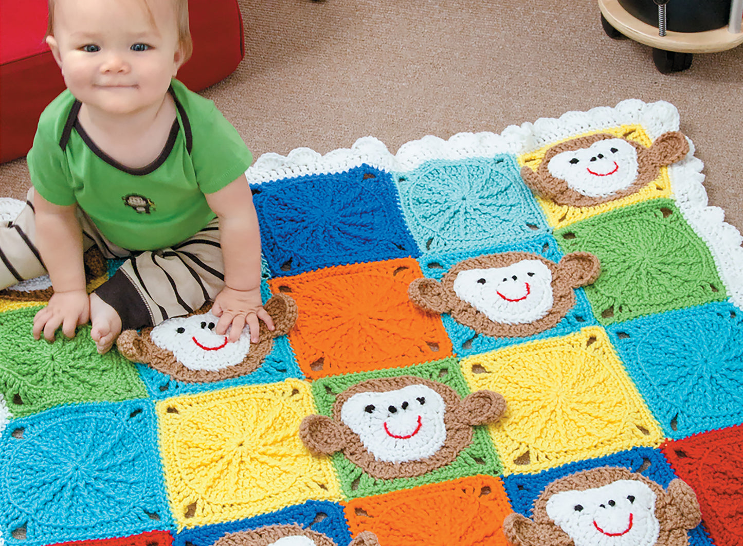 A baby in a green shirt sits on a vibrant crocheted blanket from the Crochet Bright Baby Blankets Digital Download by Leisure Arts, featuring cheerful monkey faces on colorful squares—an adorable and creative baby blanket pattern.