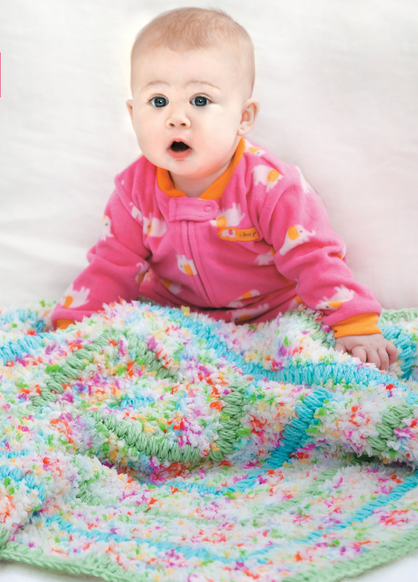 A baby in a pink onesie sits on the Crochet Bright Baby Blankets from Leisure Arts, featuring charming crochet designs. The soft, colorful blanket and white background create a bright and cozy atmosphere. Digital download available.