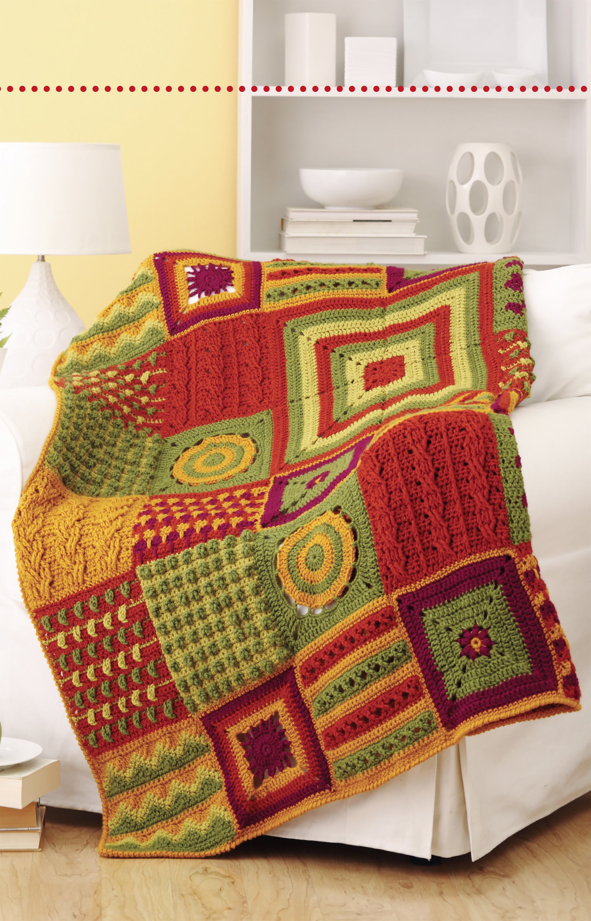 A vibrant afghan featuring green, yellow, orange, and red squares is draped over a white sofa, highlighting creative patterns from the Granny Square Stitch Guide by Leisure Arts—perfect for anyone seeking unique crochet ideas.