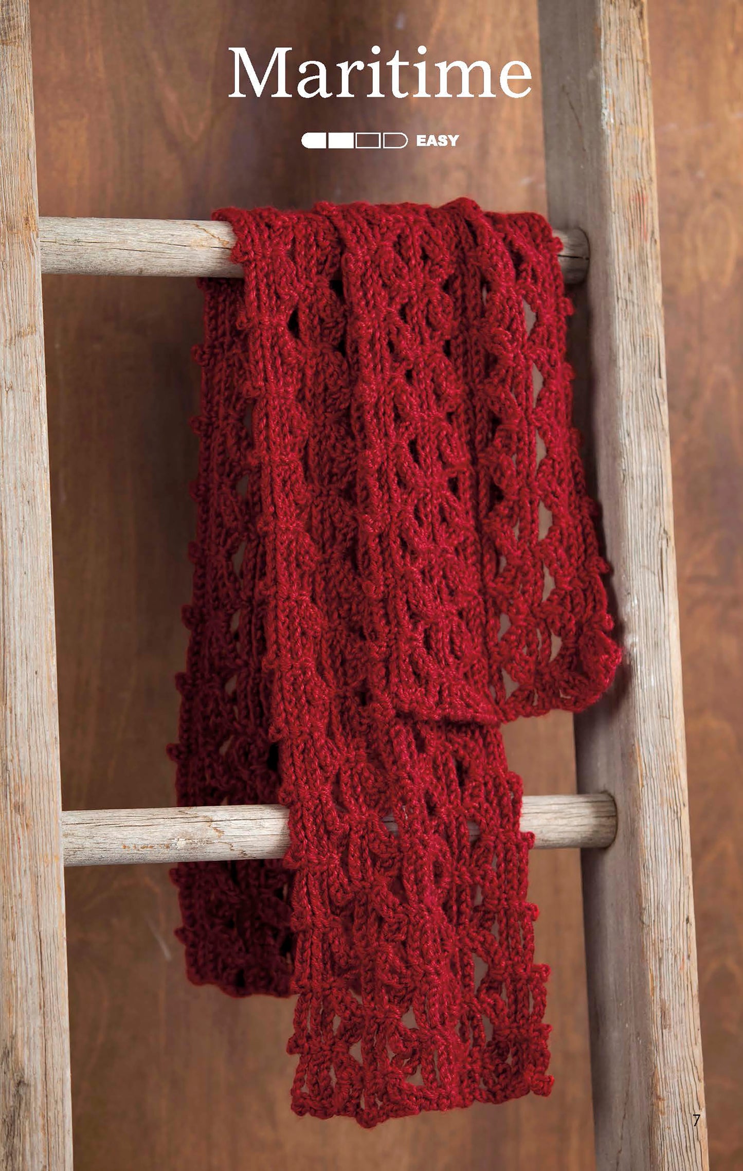 A red, lacy scarf from The Little Encyclopedia of Crocheted Scarves Digital Download by Leisure Arts hangs on a rustic wooden ladder, with “Maritime” and an easy level indicator above on a warm brown wood background.