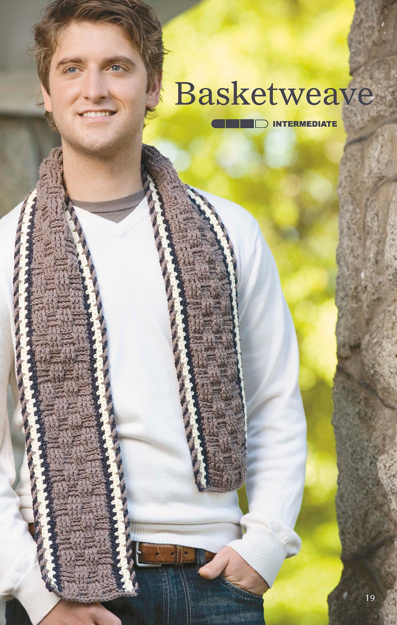 A man in a white sweater and jeans smiles outdoors, wearing a brown basketweave scarf with white and dark edges from The Little Encyclopedia of Crocheted Scarves by Leisure Arts. “Basketweave” and “Intermediate” skill level are also shown in text.