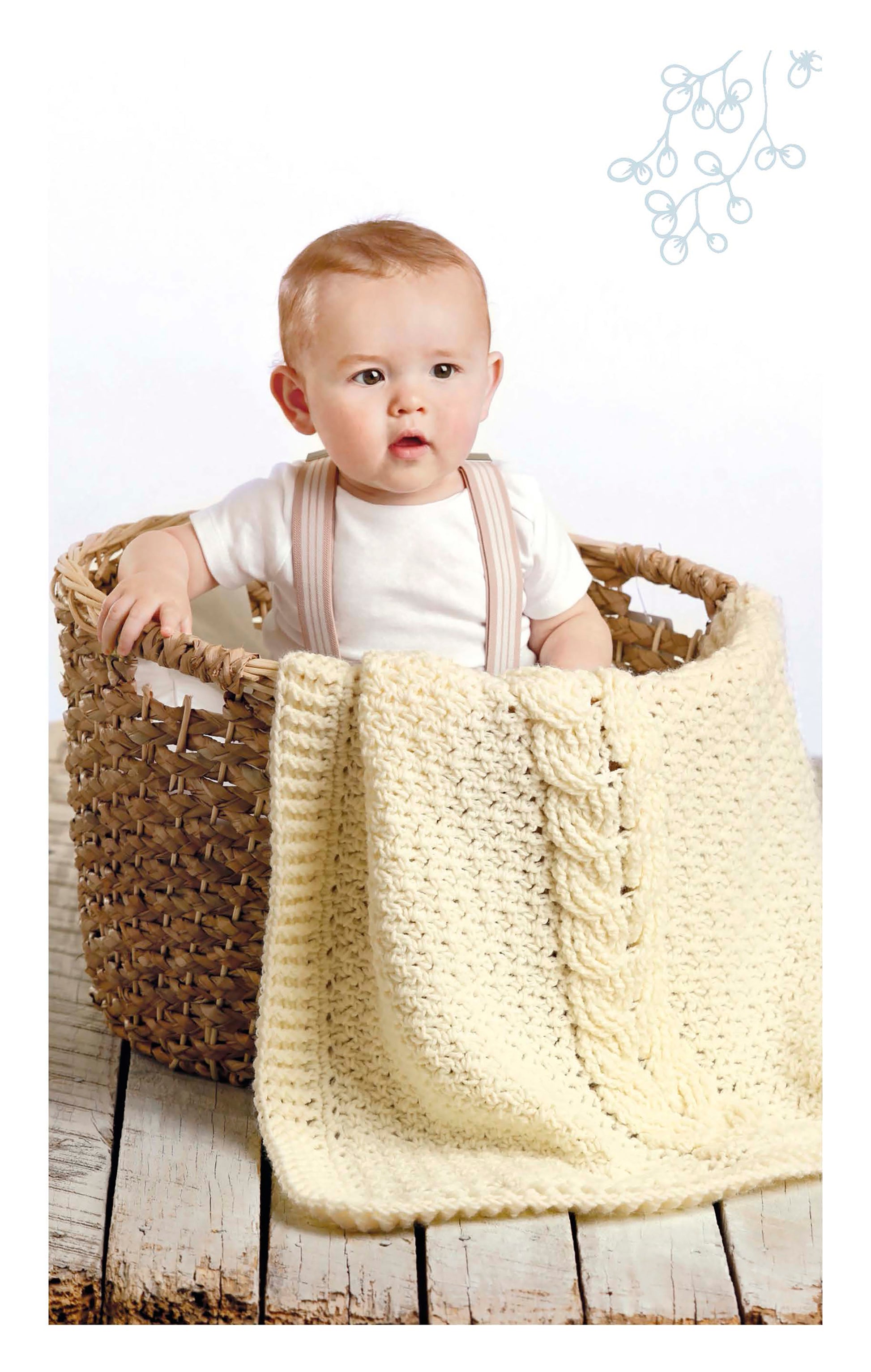 A baby in a white outfit sits in a wicker basket on a wooden floor, cozy under a Cabled Baby Blanket by Leisure Arts. The plain white background features a light blue swirl design in the top right corner.