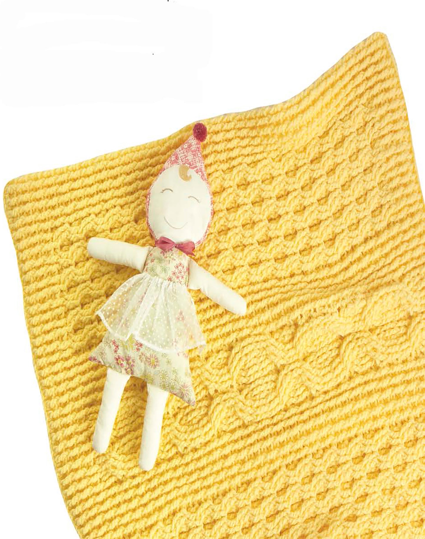 A cheerful cloth doll in a floral dress and pink hat rests on the Cabled Baby Blankets by Leisure Arts, a soft, yellow, worsted weight blanket with a textured pattern—an inviting choice for intermediate crochet enthusiasts.