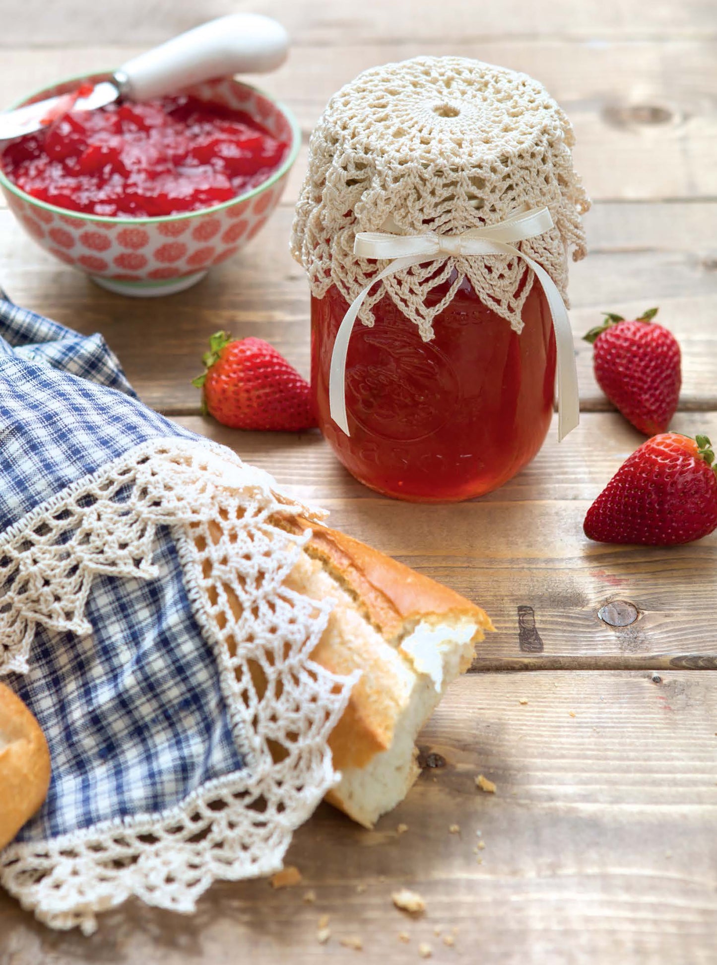 A jar of strawberry jam sits by fresh strawberries, a bowl of jam, and bread—ideal inspiration for charming home decor or beginner crochet projects. Find patterns in the Quick Thread Projects Digital Download by Leisure Arts.