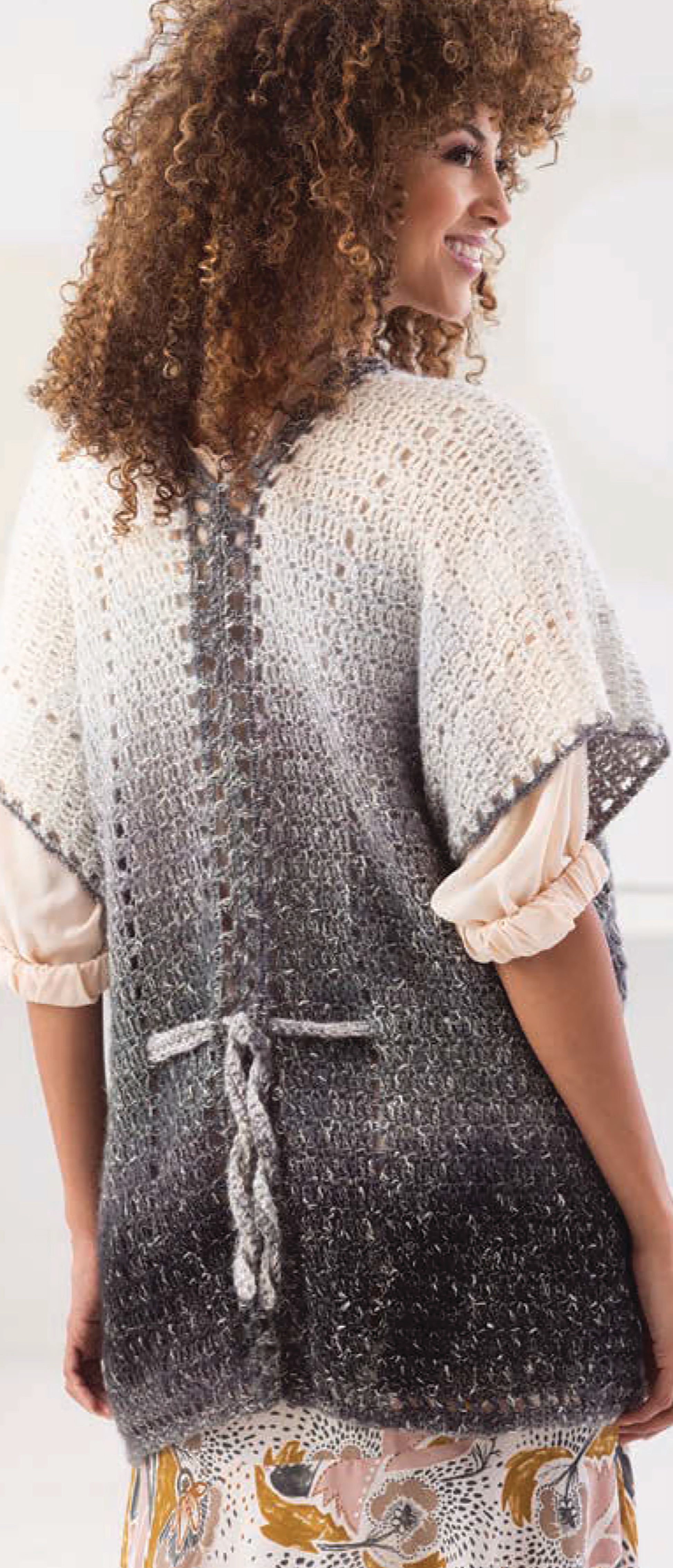 A woman with curly hair models a Leisure Arts "Shawls & Vests—Crochet 7 Bohemian Designs" poncho, featuring gradient cream to dark gray crochet patterns, lace-up back detailing, and a waist tie, over a blouse and patterned skirt.