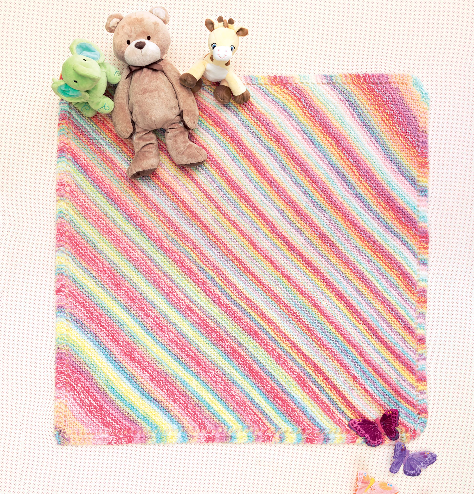 The Ice Cream Baby Afghans Digital Download by Leisure Arts features a pastel rainbow-striped knitted baby blanket spread out flat with three stuffed animals in one corner and two purple butterflies in the opposite corner.