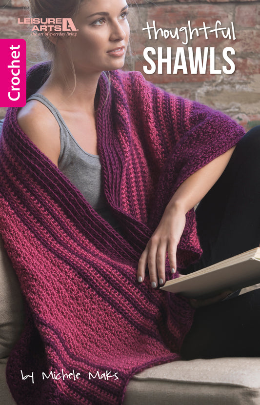 A woman relaxes on a couch wearing a striped purple and magenta crochet shawl, holding an open book. The cover for Thoughtful Shawls by Leisure Arts highlights handmade comfort and beginner-friendly crochet inspiration.