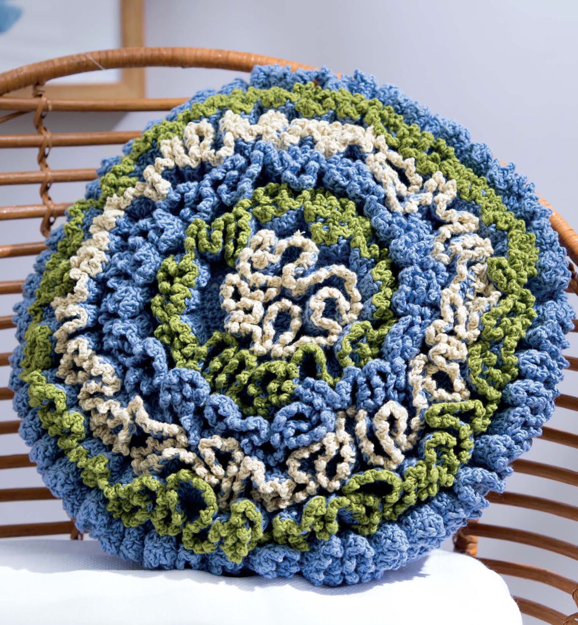 The Leisure Arts Textured Pillows Crochet features a round, ruffled cushion in blue, green, and cream with spiral crochet designs—an inspiring accent for your next pillow pattern project.