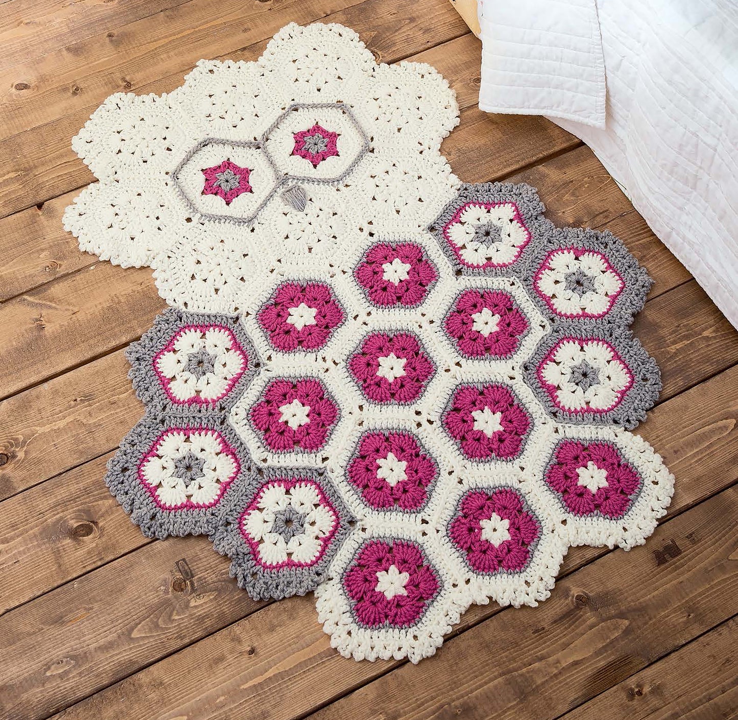The Leisure Arts Crochet Rugs for Kids features a hexagon design with white, pink, gray, and purple floral motifs—ideal playroom decor or a charming children’s gift to brighten any space.