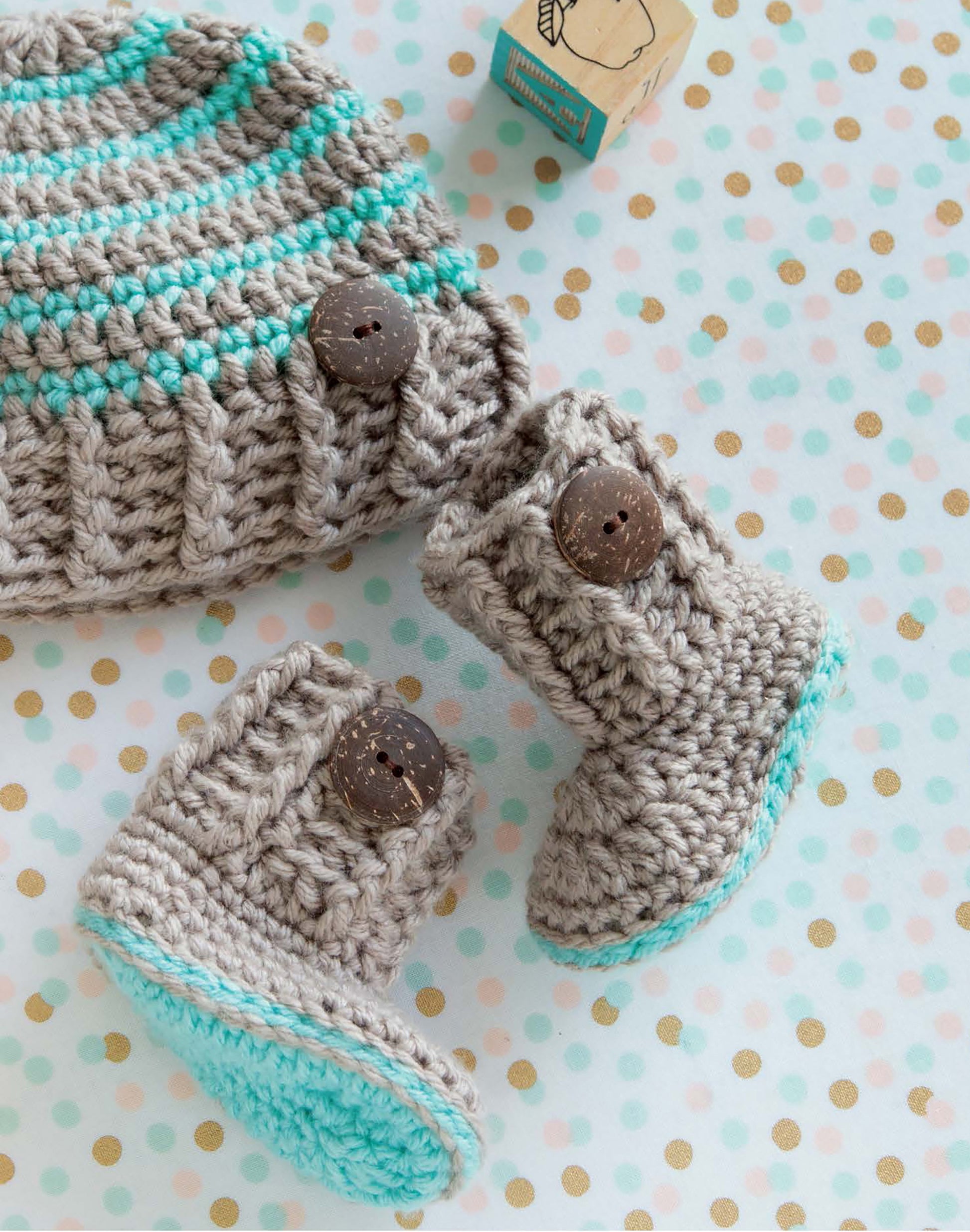 Leisure Arts Infant Boots & Hats in grey with turquoise stripes and brown buttons are showcased on a polka dot background—ideal for modern baby style or as beginner crochet shoe inspiration.
