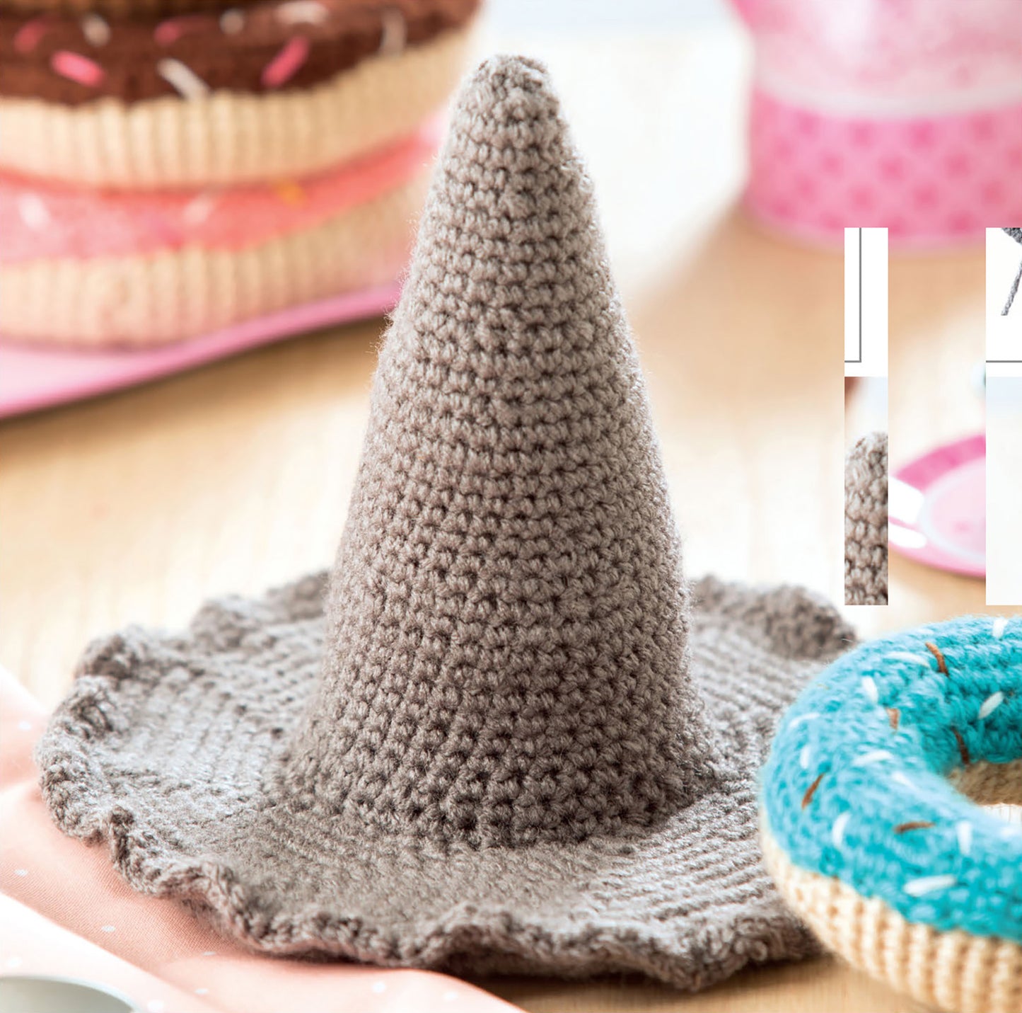 The Baby Stacks—6 Easy Toys to Crochet! kit by Leisure Arts features colorful crochet toys resembling donuts, displayed with a gray witch hat—perfect for inspiring beginner-friendly crochet designs and playful decor.