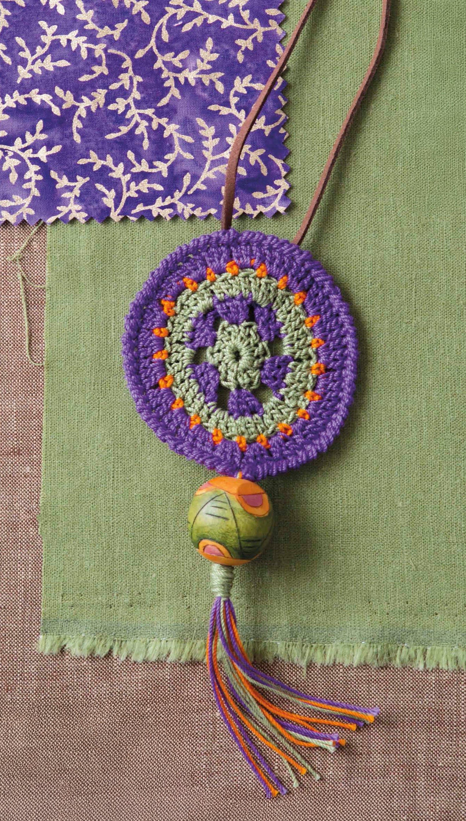Artisan Jewelry—9 Easy & Stylish Accents in Thread by Leisure Arts features a handmade crochet pendant with a circular purple-green pattern, orange accents, green bead, and multicolored tassel—great for pairing with bracelets or earrings.