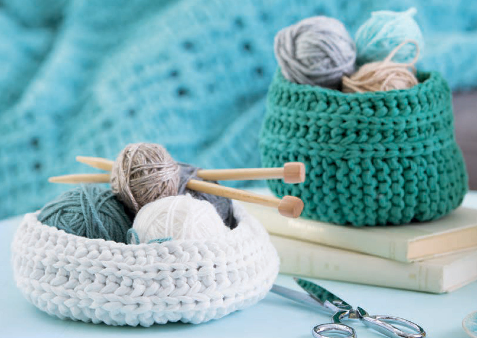 The Chunky Home Decor Digital Download by Leisure Arts features two knitted baskets, one white and one green, ideal for storing home accessories or bulky yarn. Displayed with knitting tools, they're perfect for organizing your craft space.