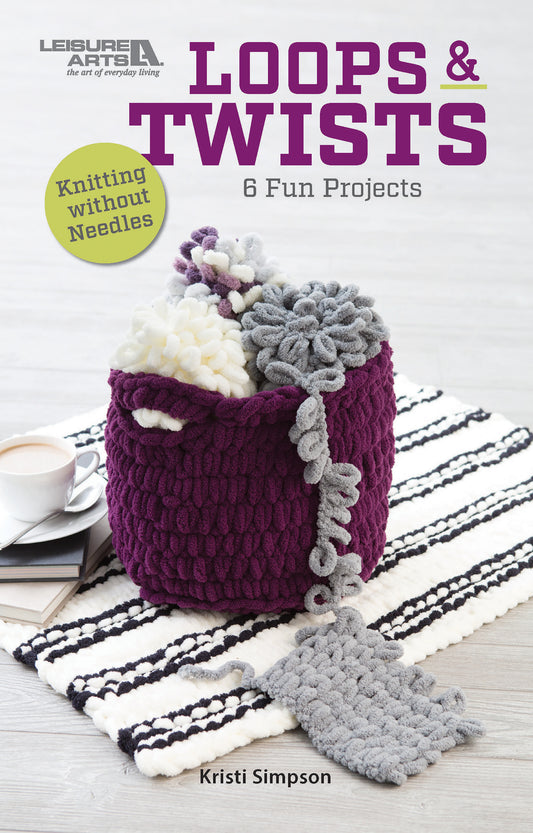 A purple textured yarn basket filled with chunky loop yarn and beginner knitting projects from Leisure Arts’ Loops & Twists—Knitting Without Needles sits on a striped rug. A cup and saucer are beside it. Text: “6 Fun Projects, Kristi Simpson.”.