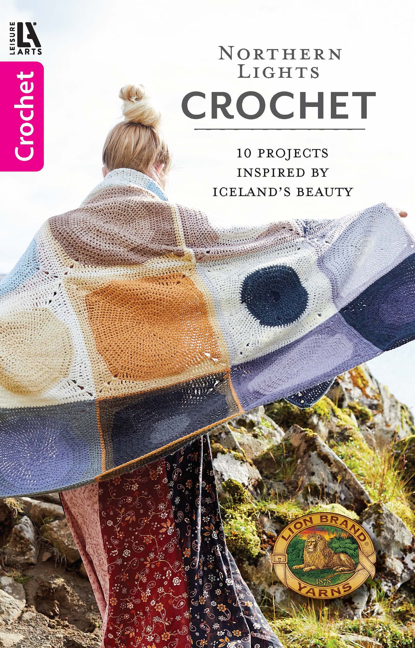 A person outdoors is wrapped in a vibrant geometric crocheted blanket. Text: Northern Lights Crochet Digital Download—10 Icelandic-inspired patterns. Leisure Arts logo appears at the bottom.