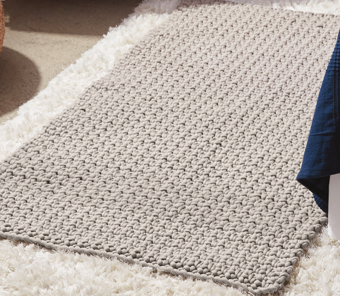 The Daydream Pattern Collection Digital Download by Leisure Arts is featured on a beige, chunky knit rug over a fluffy white carpet, with a blue blanket partially visible in the upper right corner.