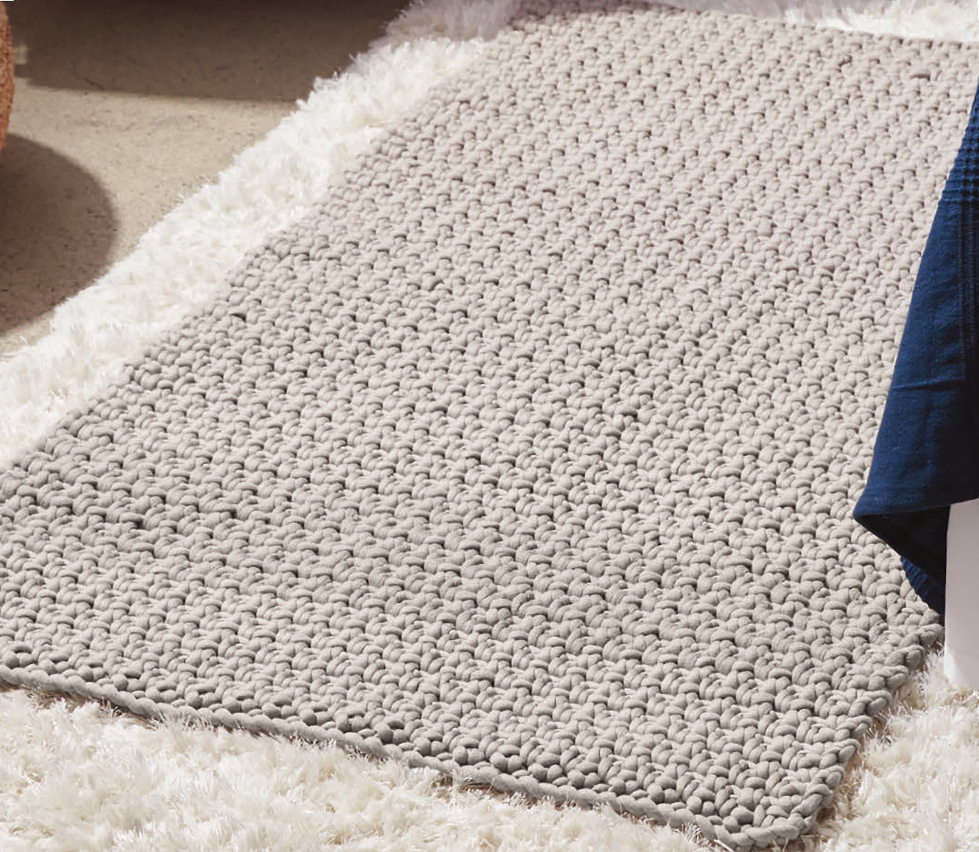 The Daydream Pattern Collection Digital Download by Leisure Arts is featured on a beige, chunky knit rug over a fluffy white carpet, with a blue blanket partially visible in the upper right corner.