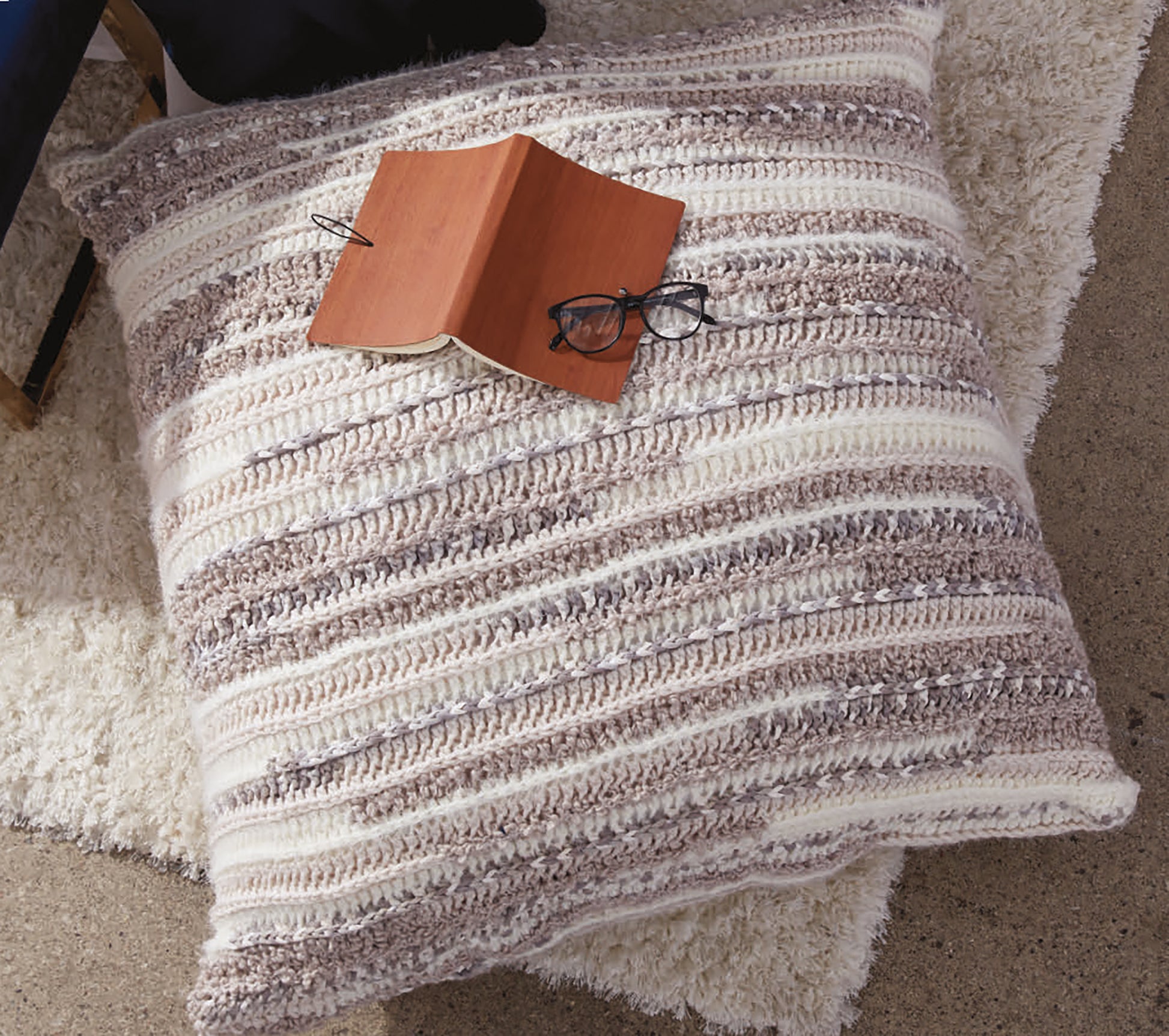 A large, striped crochet pillow made with bulky yarn sits on a cream rug next to the Daydream Pattern Collection Digital Download by Leisure Arts—an inviting setup perfect for cozy crochet and knit inspiration.