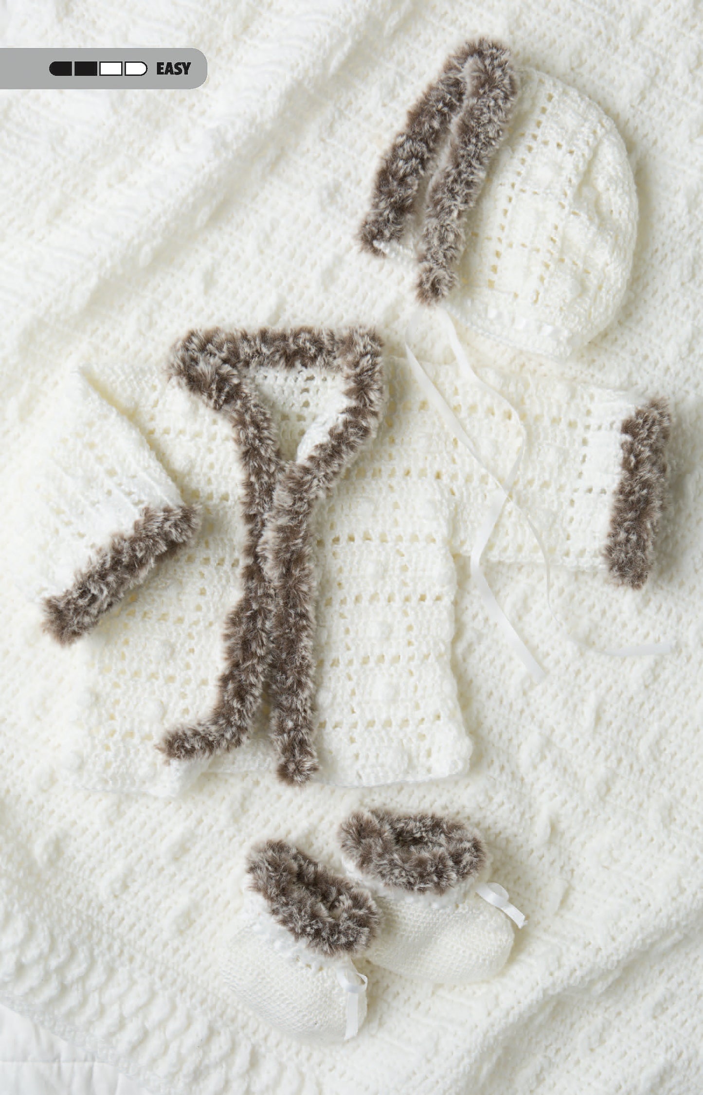 The Crochet Tiny Tot Accessories set by Leisure Arts features a white knitted baby cardigan, hat, and booties with fluffy brown trim—cozy essentials for infants and a charming example of easy baby crochet projects.