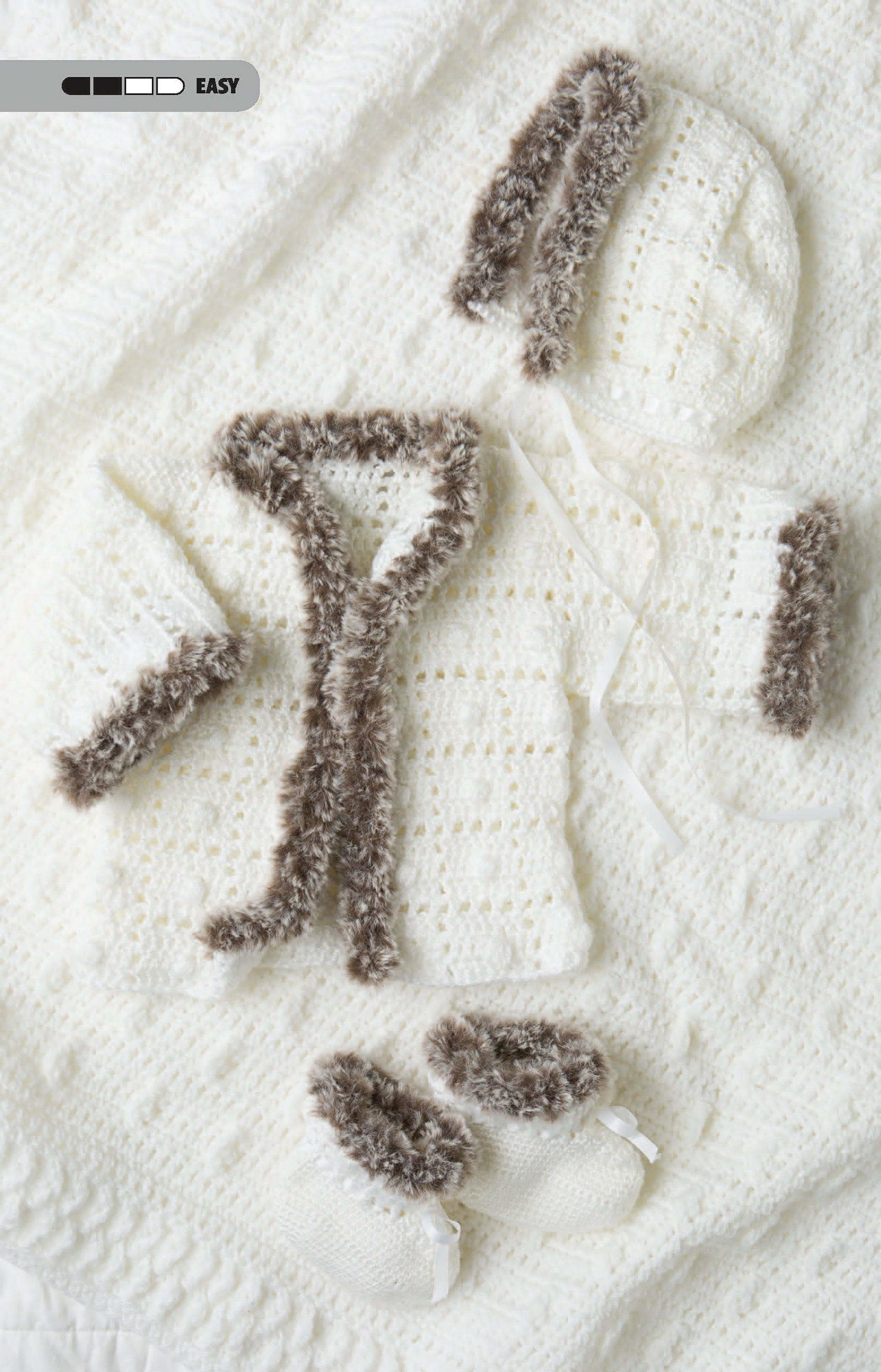 The Crochet Tiny Tot Accessories set by Leisure Arts features a white knitted baby cardigan, hat, and booties with fluffy brown trim—cozy essentials for infants and a charming example of easy baby crochet projects.