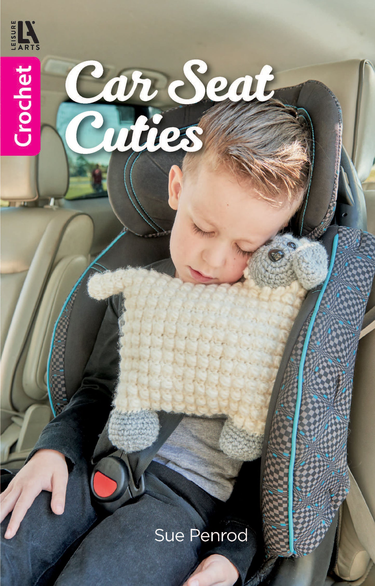A young boy sleeps in a car seat, cuddling a crocheted sheep pillow beside the book Car Seat Cuties by Leisure Arts, a pocket-size crochet book featuring adorable animal patterns.